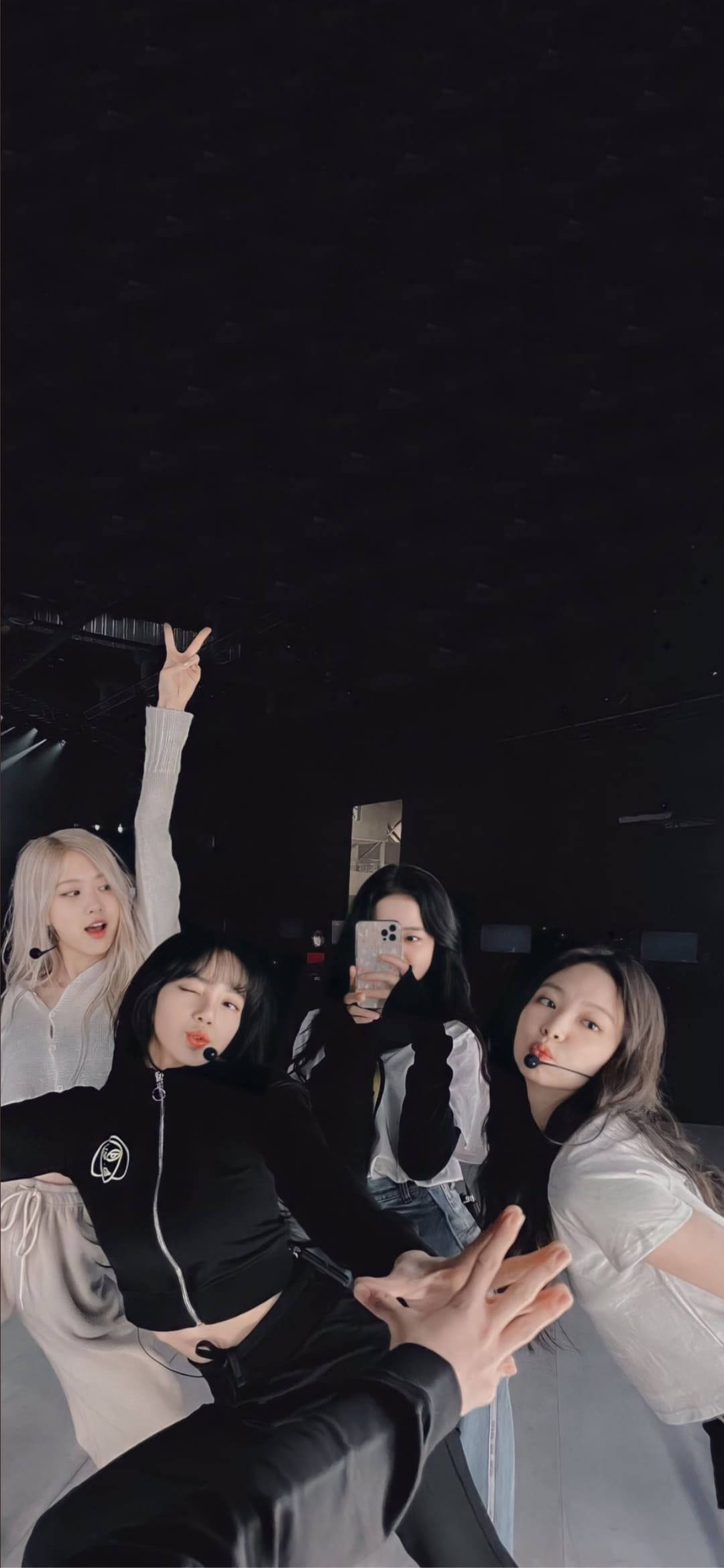 BLACKPINK 桌布 壁紙 — 四位年輕女性穿著表演服裝，在昏暗的舞台燈光下，一隻手伸向鏡頭，俏皮地自拍。