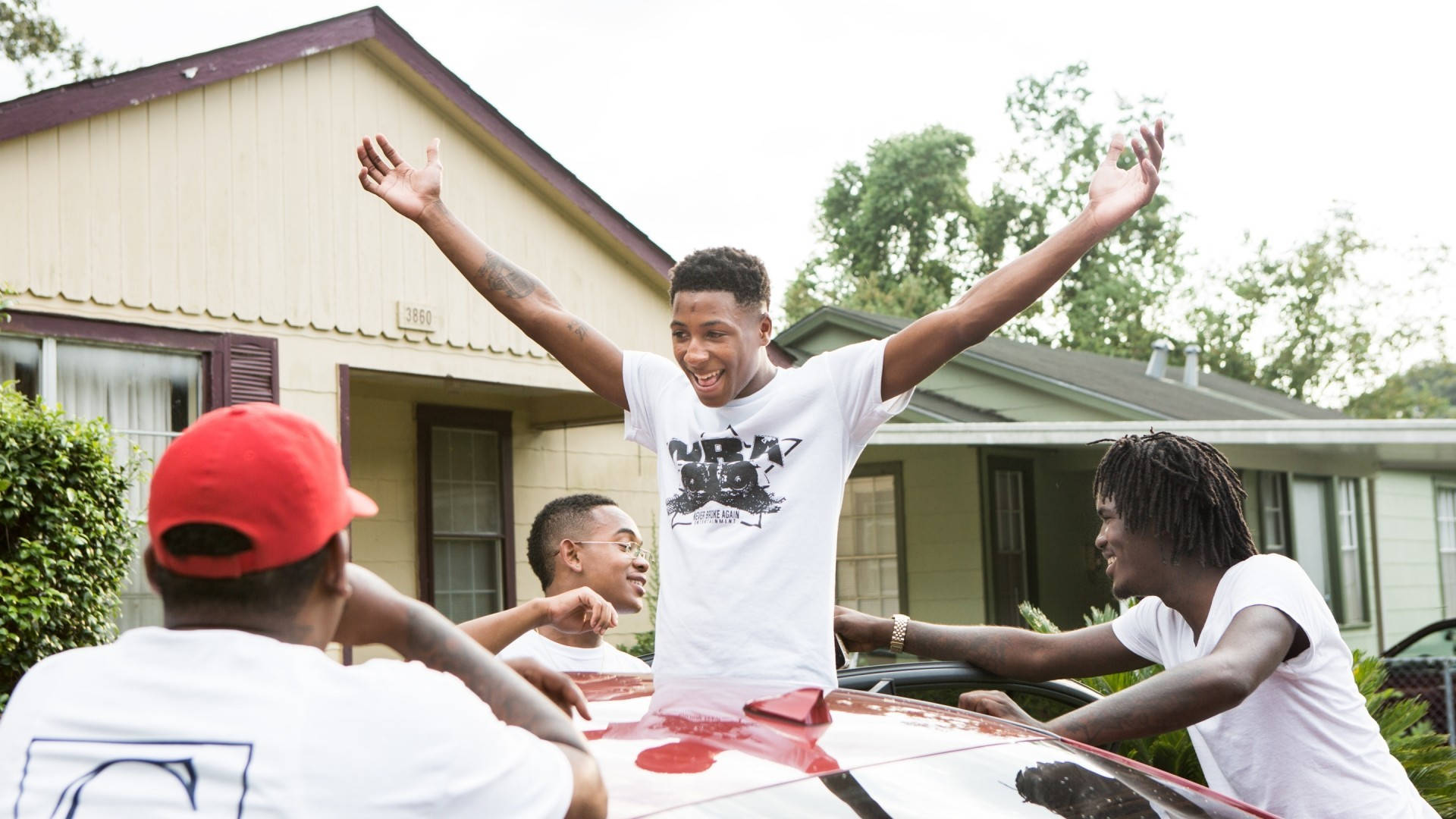 Youngboy 桌布 壁紙 — 四位年輕男子在郊區住宅區圍繞一輛紅色汽車，高舉雙臂，笑容燦爛地慶祝。