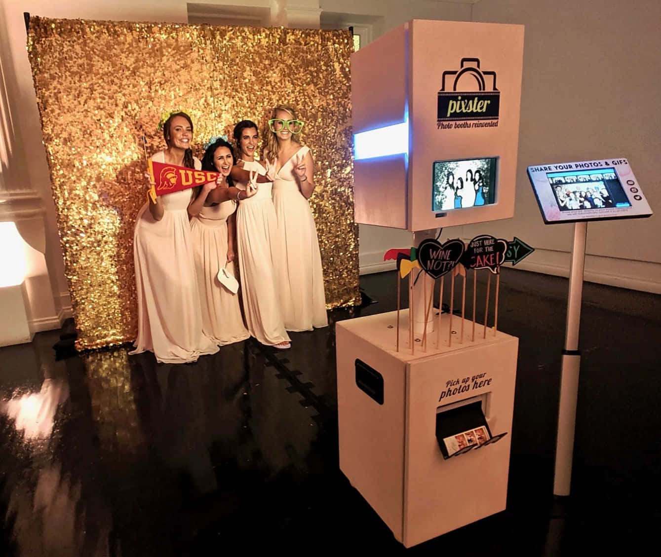 Photo Booth 桌布 壁紙 — 四位微笑的女性穿著奶油色連衣裙，在閃閃發光的金色背景前於拍照亭活動中愉快地擺姿勢。
