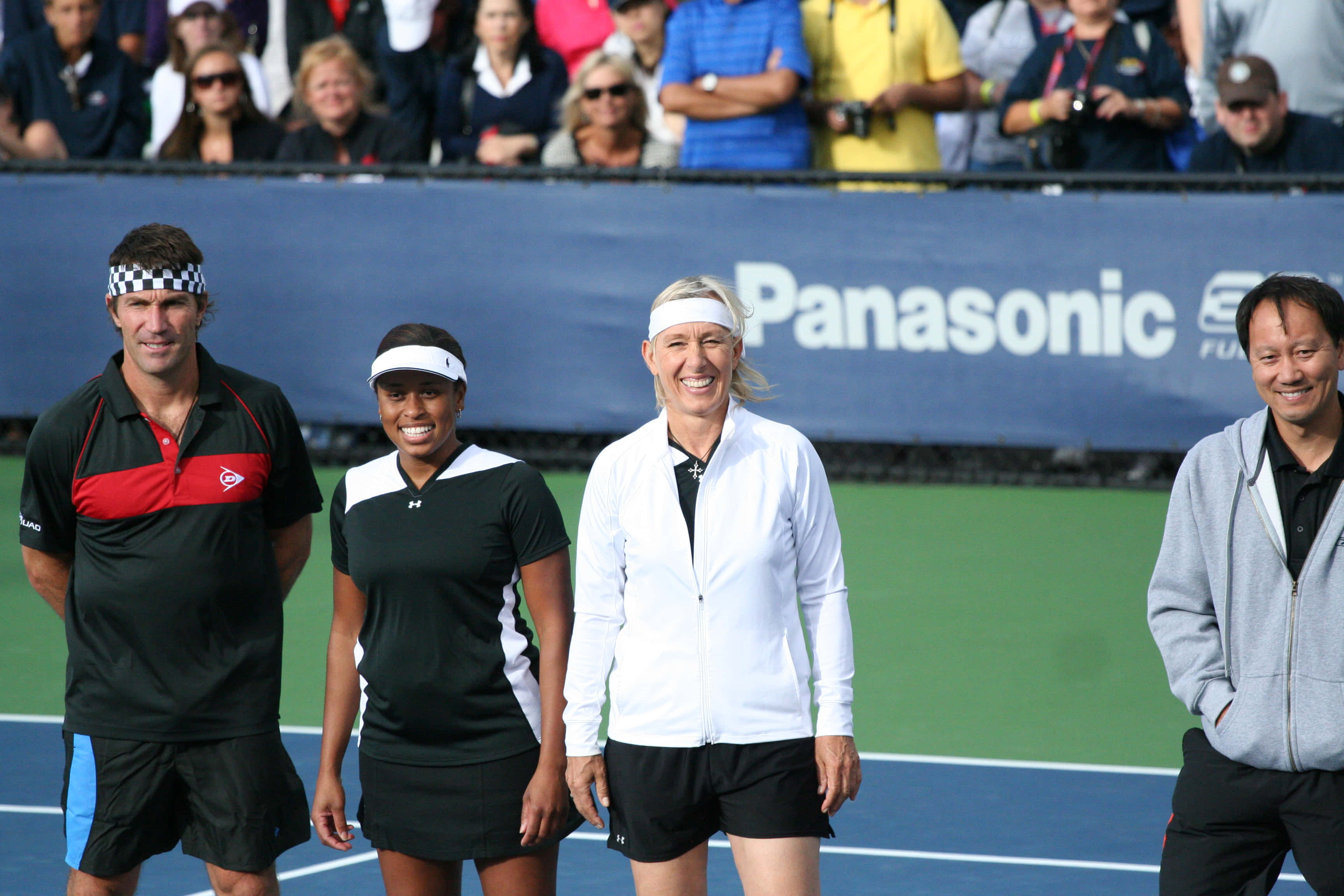 Tennis 桌布 壁紙 — 四位微笑的網球選手和裁判站在藍色硬地球場上，背景有觀眾。