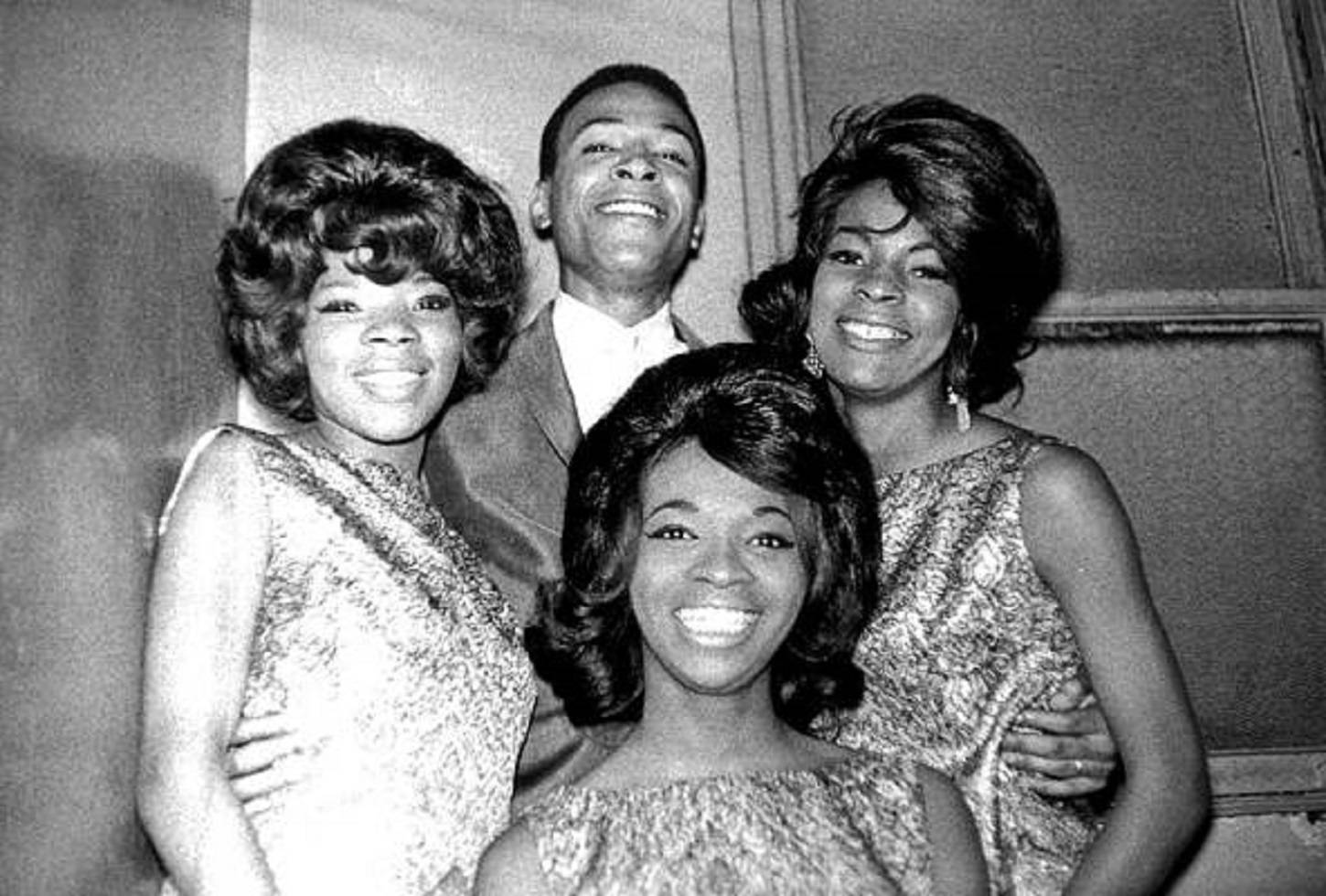 Singer 桌布 壁紙 — 四位微笑的至上女聲組合（The Supremes）成員身穿1960年代華麗服裝，在室內素牆前緊密擺姿勢。