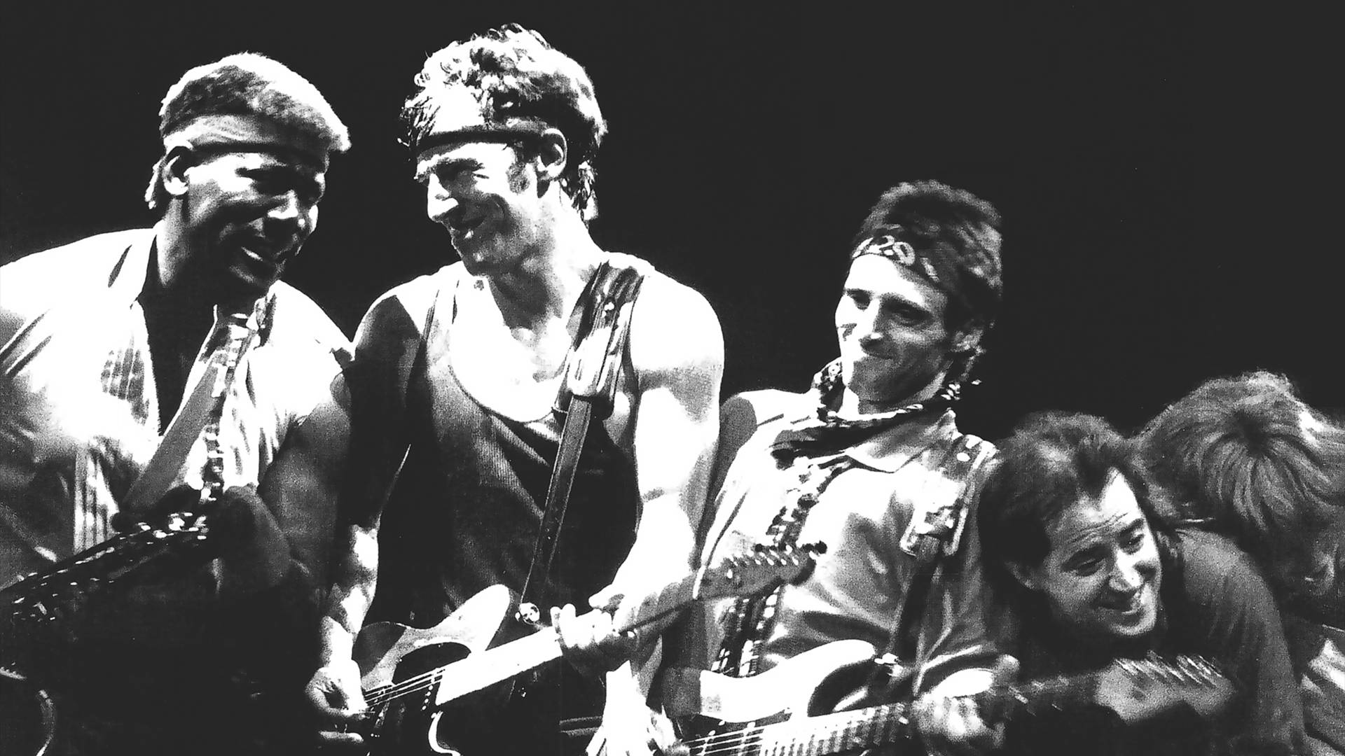 Bruce Springsteen 桌布 壁紙 — 四位微笑的音樂家在明亮聚光燈下於舞台上彈吉他的黑白照片。