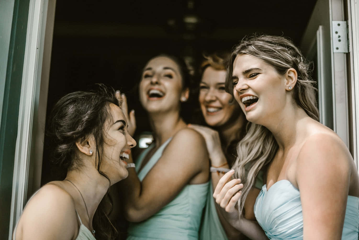 Bridal 桌布 壁紙 — 四位快樂的伴娘穿著淺藍色連衣裙，在溫暖照明的門口一起大笑。