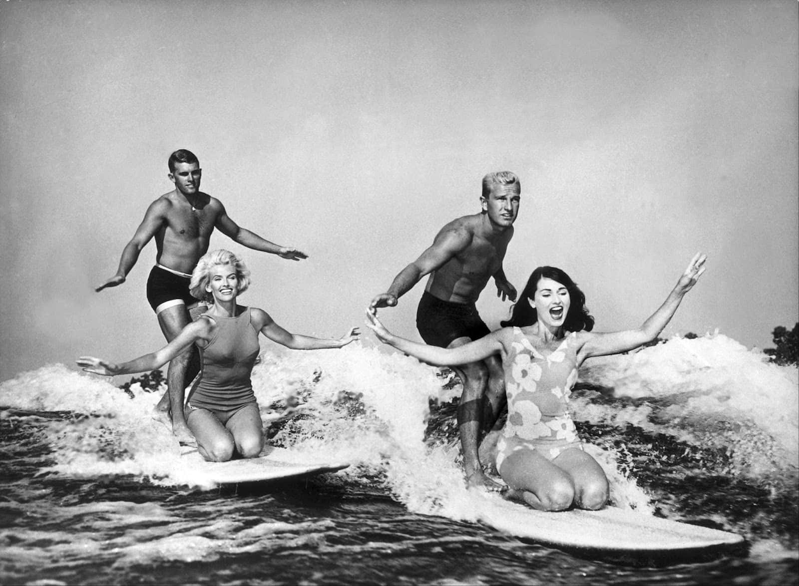 Vintage Surf 桌布 壁紙 — 四位快樂的衝浪者張開雙臂乘風破浪，經典黑白照片。