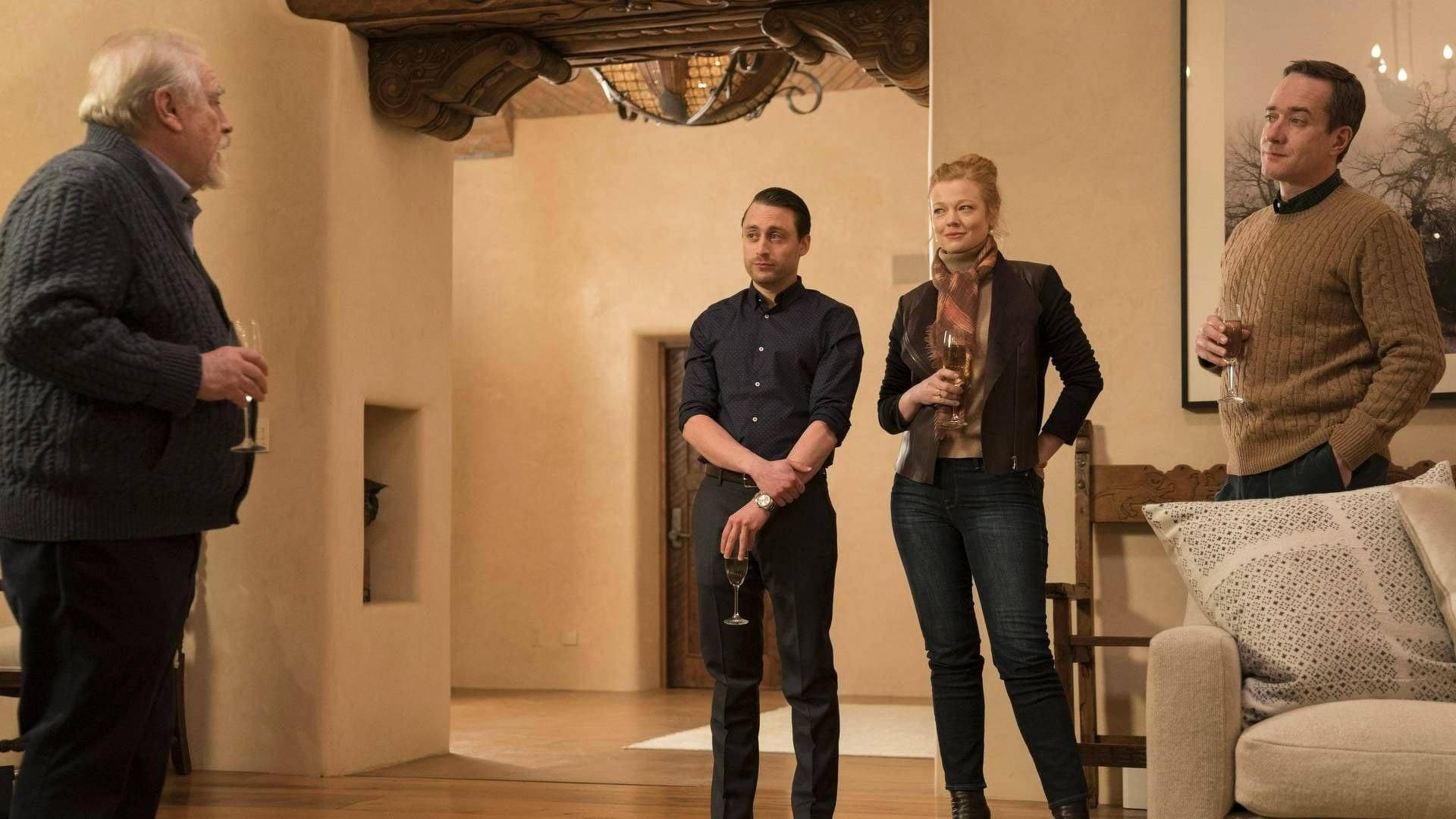 Succession 桌布 壁紙 — 四位成年人站在溫暖燈光的鄉村風格室內，在社交聚會中手持酒杯。