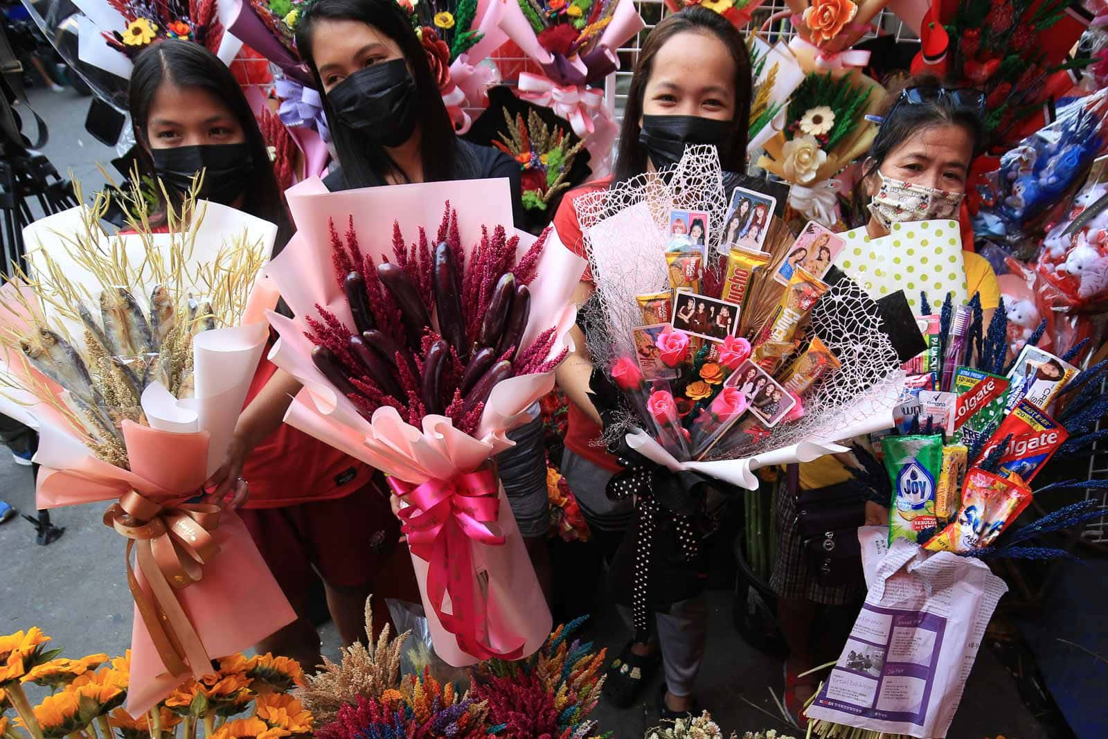 Valentine's Day 桌布 壁紙 — 四位戴著口罩的女性在充滿活力的街市攤位上自豪地展示色彩繽紛的花束和糖果。