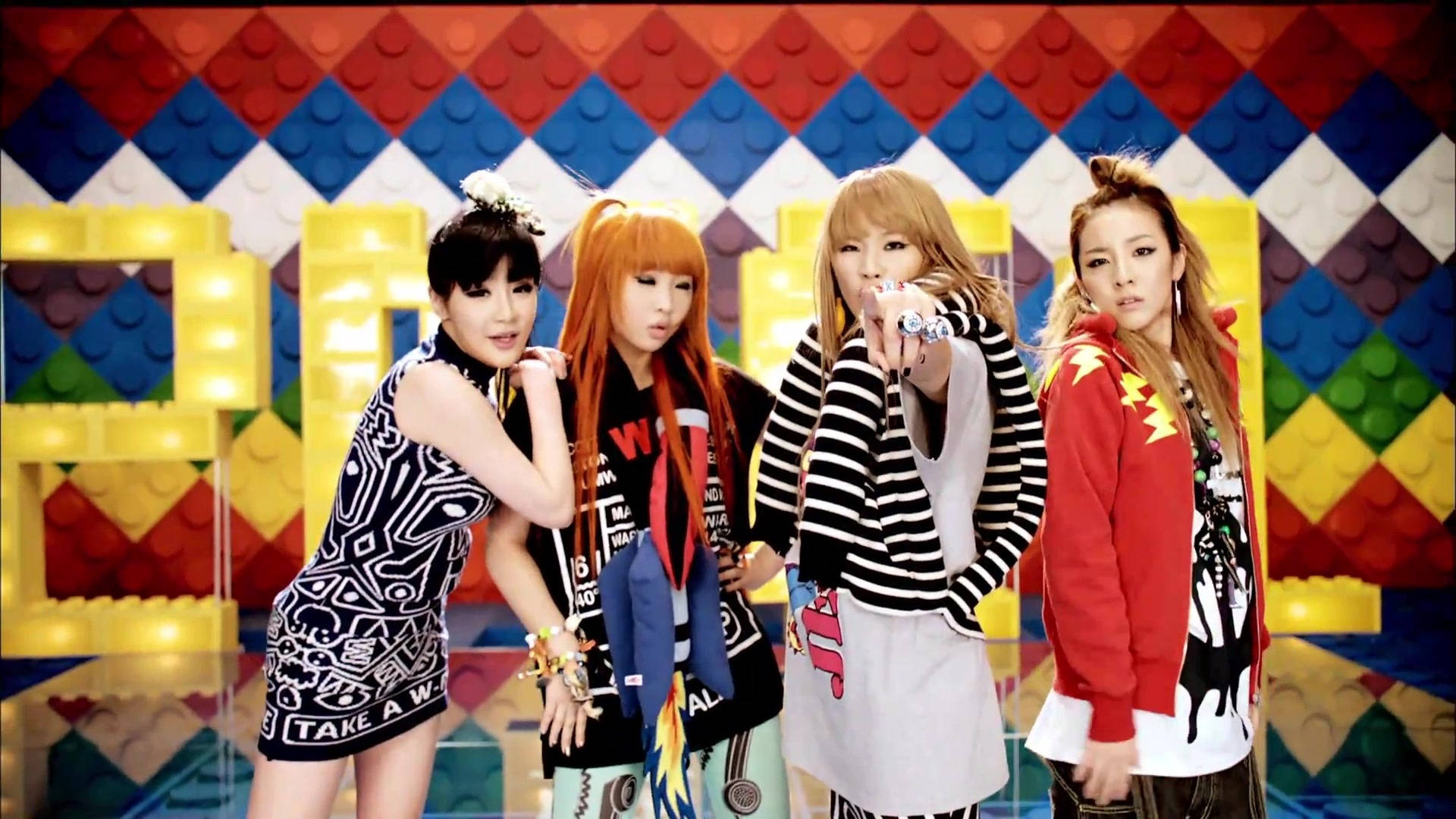 2ne1 桌布 壁紙 — 四位時尚女性在色彩繽紛的LEGO磚牆背景下自信地擺姿勢，背景有發光的黃色積木。