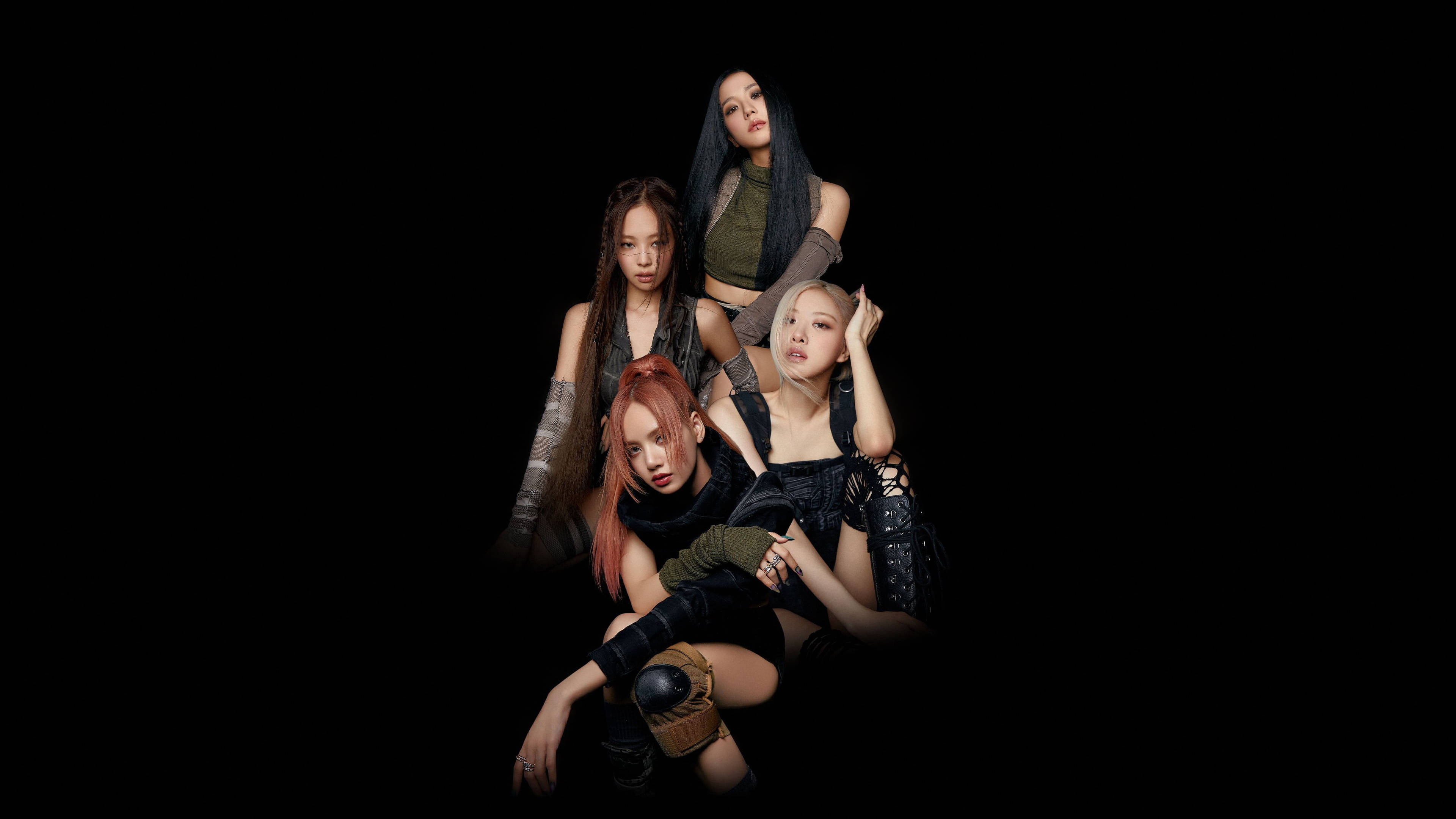 BLACKPINK 桌布 壁紙 — 四位時尚女性穿著前衛服裝，在強烈燈光下，於純黑背景前戲劇性地擺姿勢。