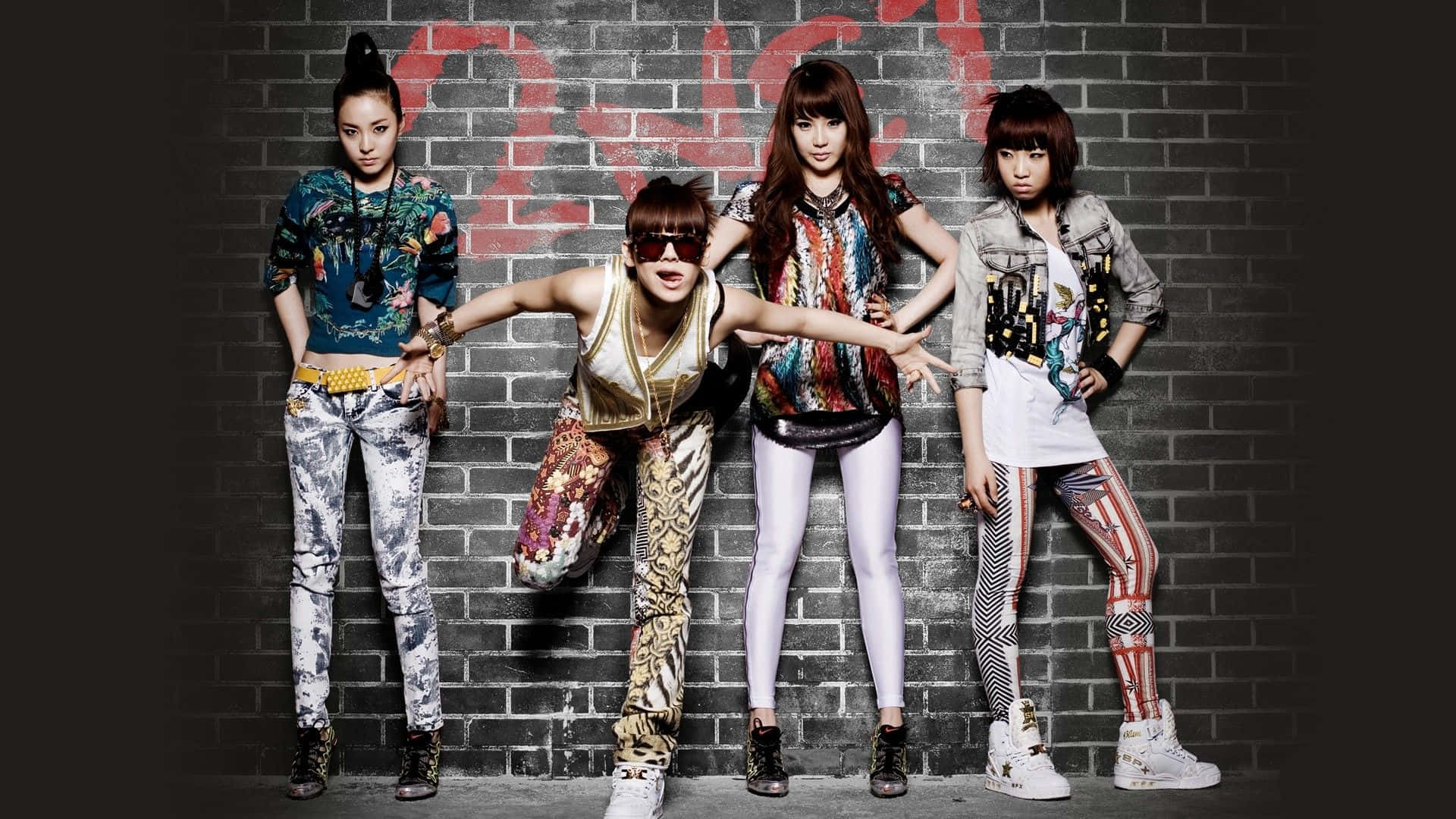 2ne1 桌布 壁紙 — 四位時尚女性穿著大膽圖案的服裝，在塗鴉覆蓋的磚牆前自信地擺姿勢。