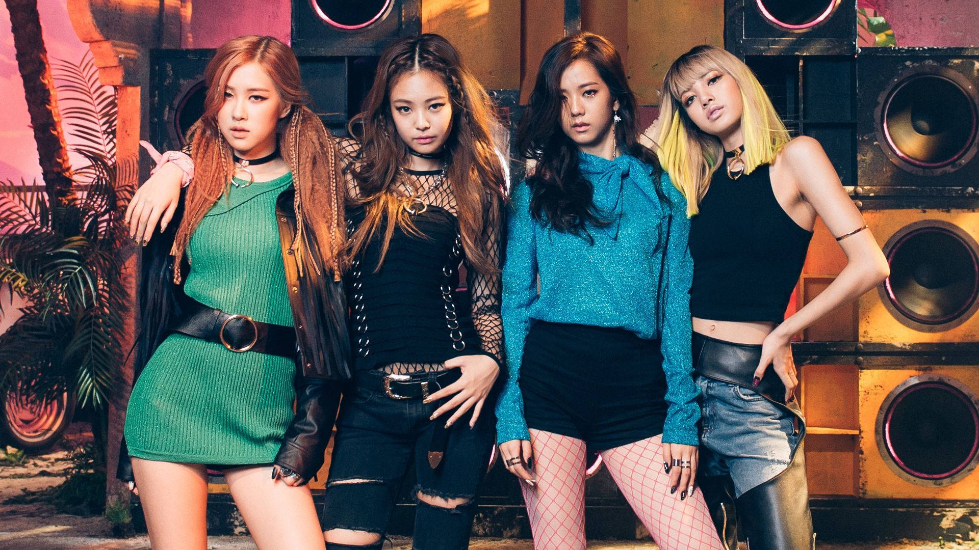 BLACKPINK 桌布 壁紙 — 四位時尚女性穿著大膽服裝，在大型揚聲器和熱帶植物的背景下，在溫暖的燈光下自信地擺姿勢。