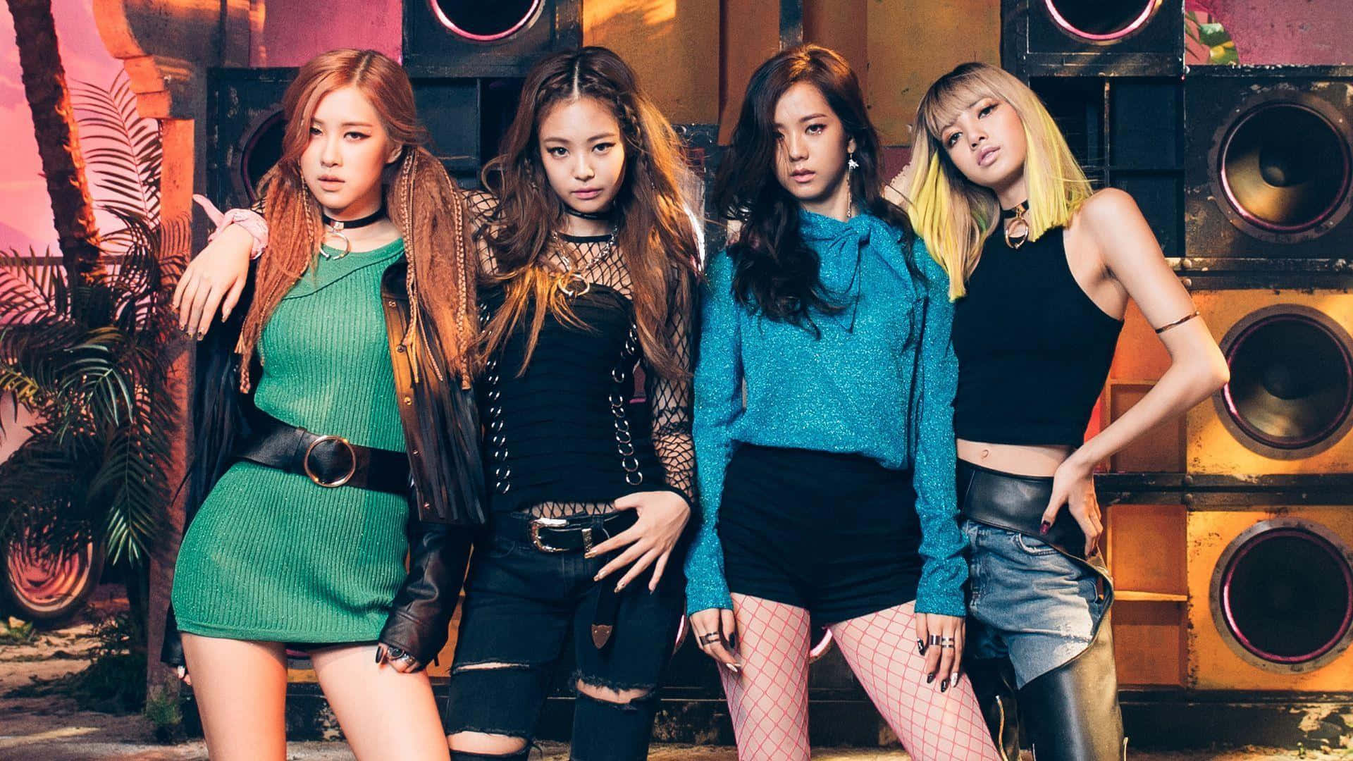 BLACKPINK 桌布 壁紙 — 四位時尚女性穿著大膽服裝，在巨型喇叭和熱帶植物背景下，於溫暖燈光下自信地擺姿勢。