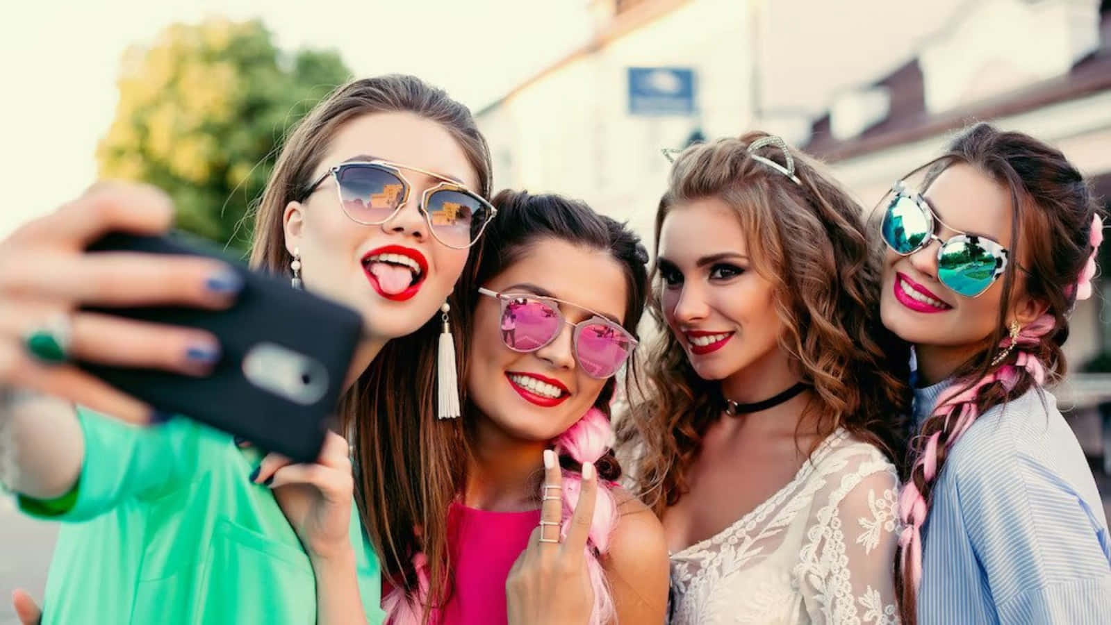 Friendship 桌布 壁紙 — 四位時尚女性穿著色彩繽紛的服裝和太陽眼鏡，在陽光明媚的街道上開心地自拍。