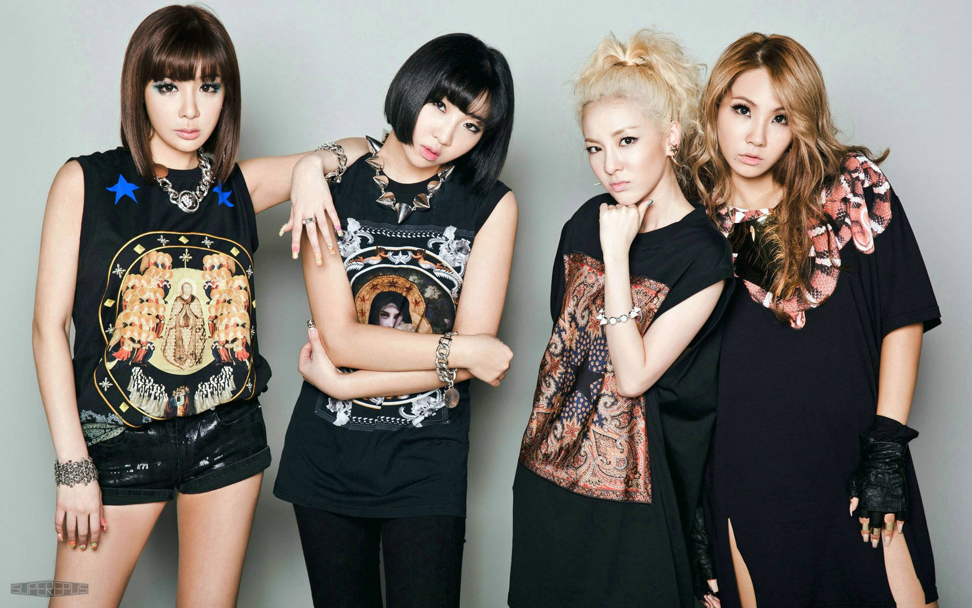 2ne1 桌布 壁紙 — 四位時尚女性自信地擺姿勢，穿著前衛的黑色服裝，帶有醒目的圖案印花，背景是純灰色攝影棚。