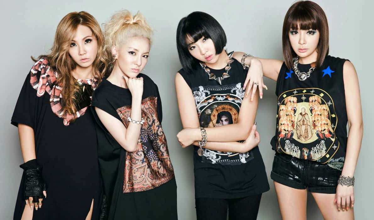 2NE1 桌布 壁紙 — 四位時尚女性自信地擺姿勢，身穿帶有醒目圖案印花的黑色服裝，背景是樸素的灰色攝影棚。