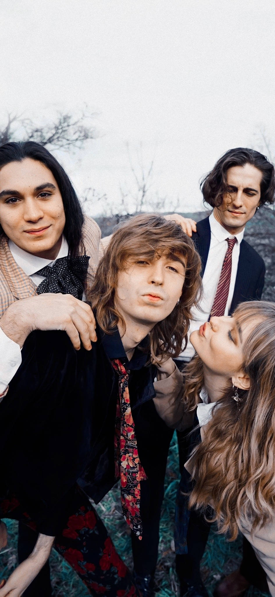 Maneskin 桌布 壁紙 — 四位時尚年輕人在陰沉多雲的戶外環境中緊密擺姿勢，背後有光禿的樹木。