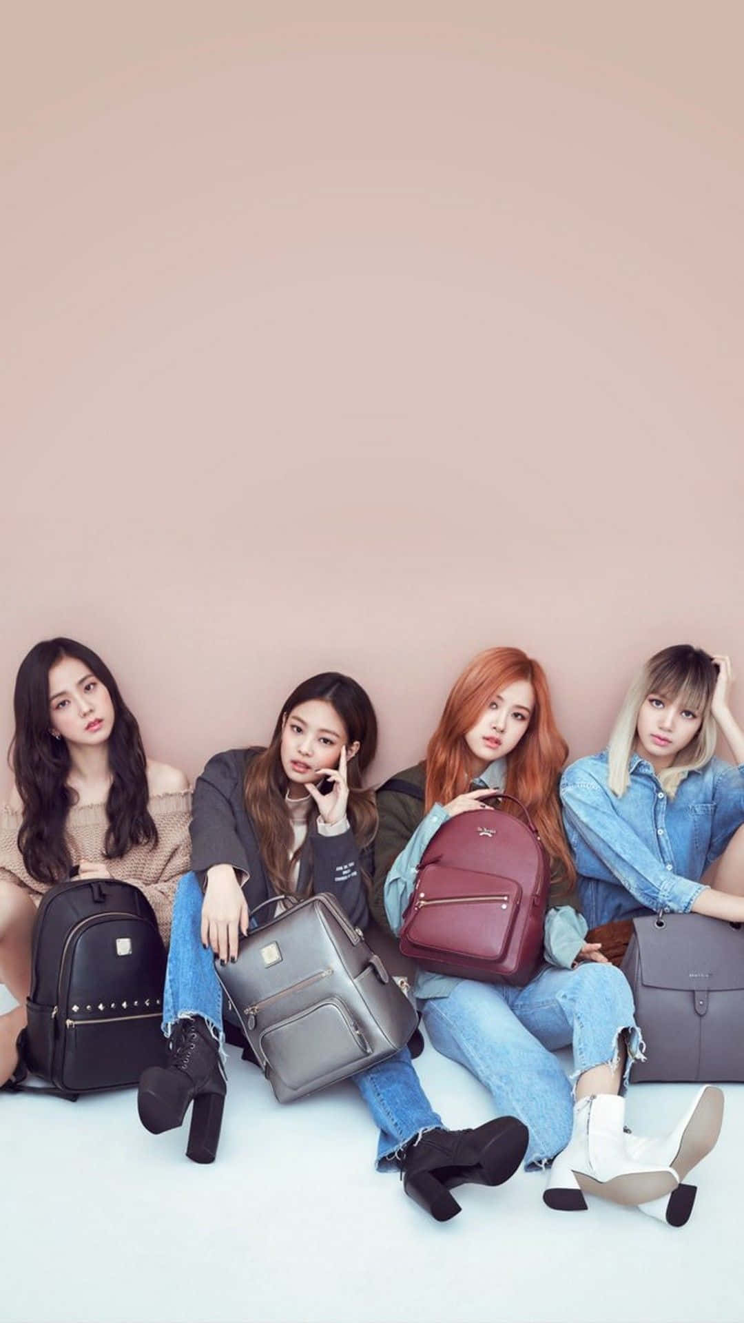 K-pop 桌布 壁紙 — 四位時尚年輕女性在白色地板上對著柔和的粉紅色牆壁隨意擺姿勢，每人手持一個設計師背包。