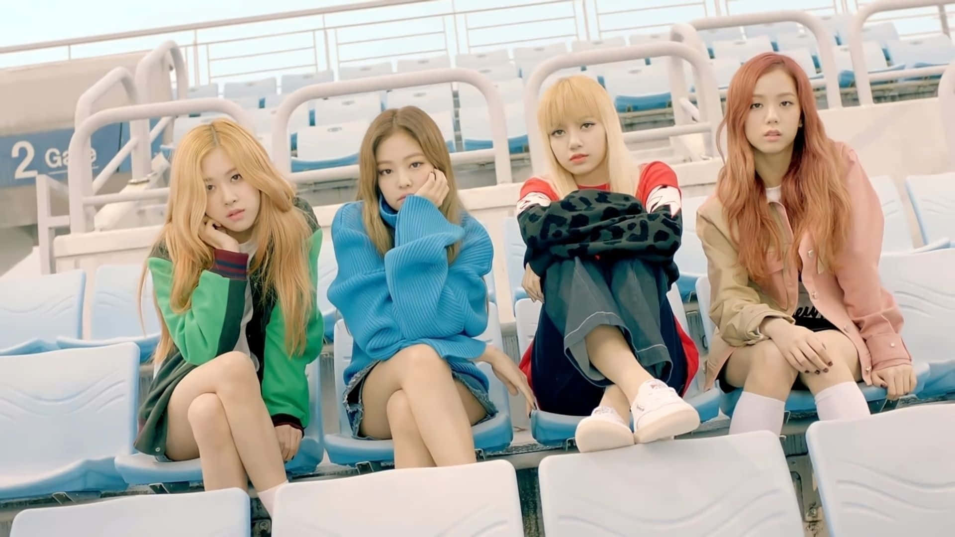 K-pop 桌布 壁紙 — 四位時尚年輕女性坐在體育場座位上，在明亮的日光下露出沉思的表情。