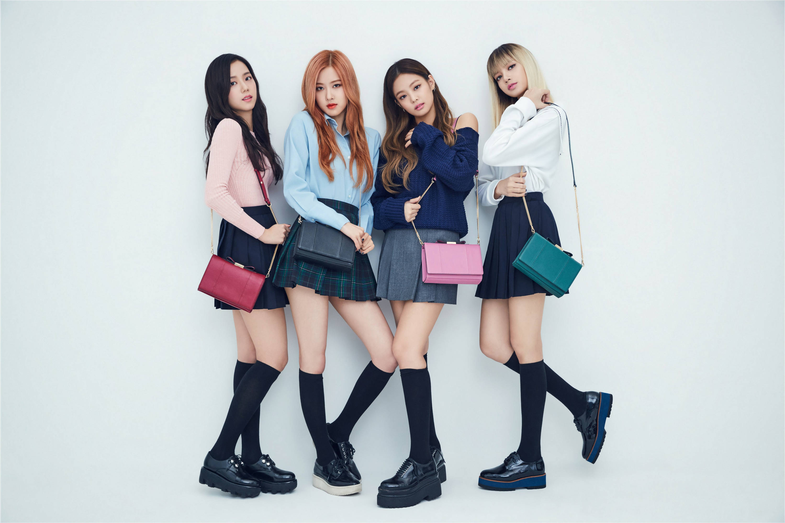 BLACKPINK 桌布 壁紙 — 四位時尚年輕女性穿著協調的校服，在純白背景前自信地擺姿勢，每人手持一個色彩繽紛的手袋。