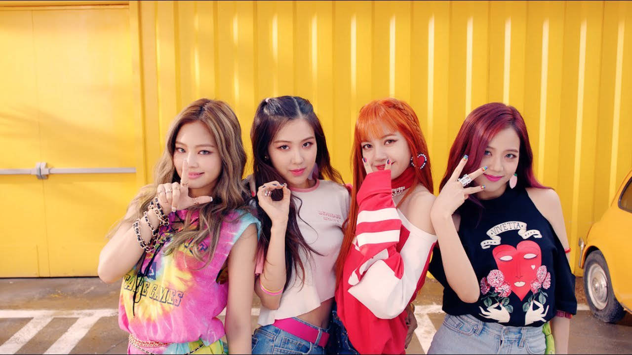 BLACKPINK 桌布 壁紙 — 四位時尚年輕女性自信地擺姿勢，背景是明亮的黃色波紋牆，一輛黃色汽車部分可見。