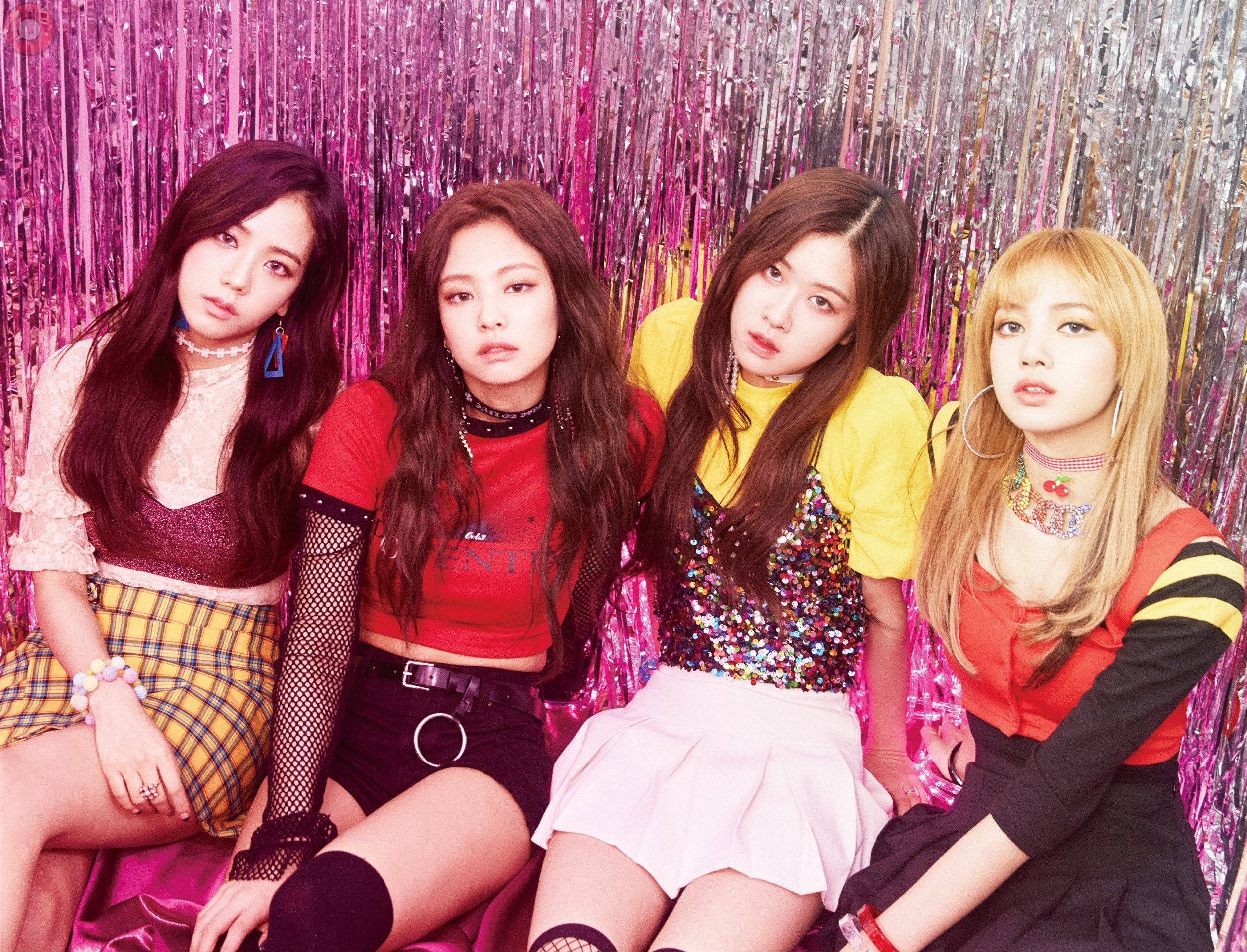 BLACKPINK 桌布 壁紙 — 四位時尚年輕女性自信地擺姿勢，背景是閃閃發光的粉紅色和銀色閃粉，穿著大膽色彩繽紛的服裝。