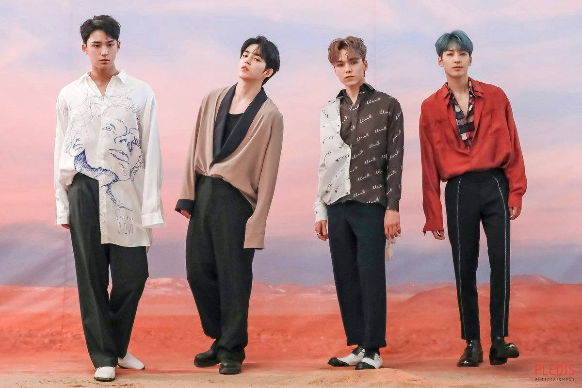 Wonwoo 桌布 壁紙 — 四位時尚男士穿著時尚服裝，自信地站在紅色沙漠景觀上超現實的粉紅色和橙色天空前。
