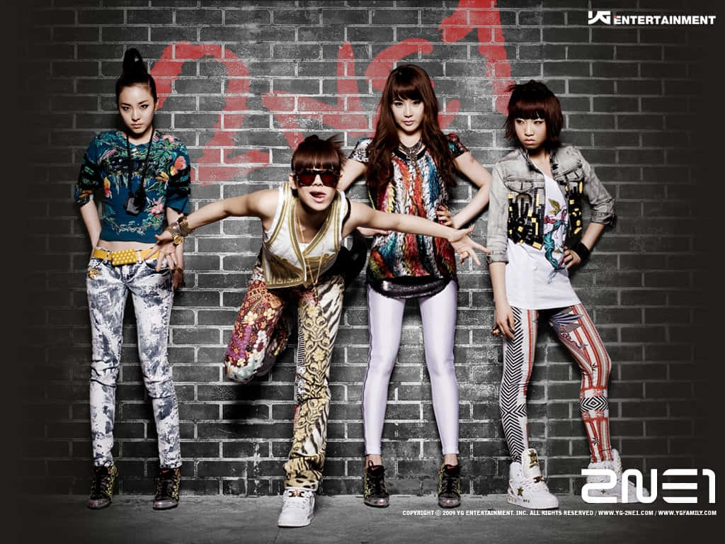2NE1 桌布 壁紙 — 四位時尚的K-pop女孩穿著大膽圖案的服裝，在塗鴉覆蓋的磚牆前自信地擺姿勢。