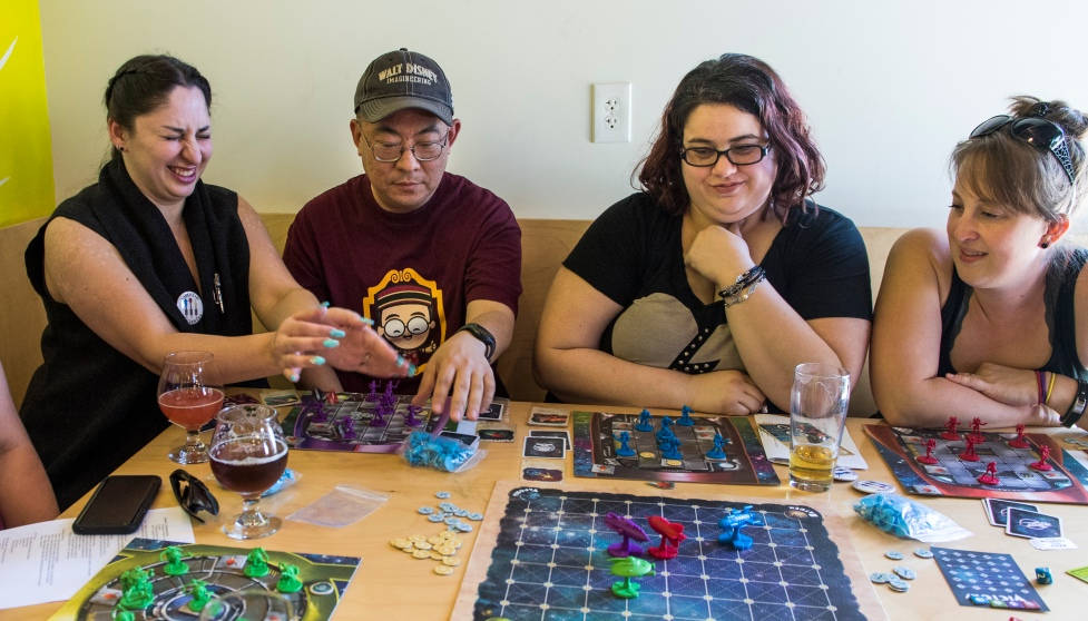 game 桌布 壁紙 — 四位朋友圍著木桌大笑，玩色彩繽紛的棋盤遊戲，並享用飲料和點心。