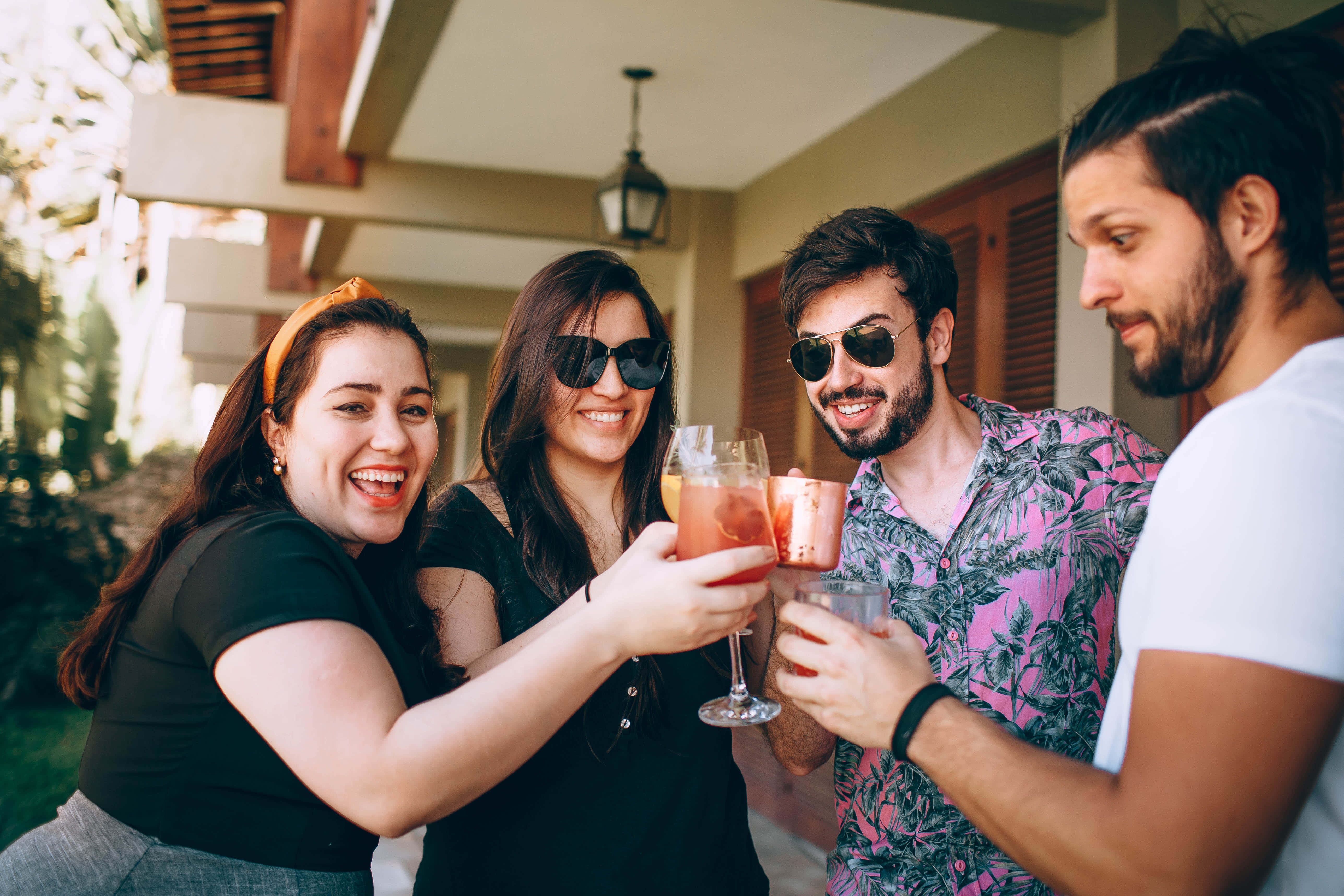 Summer Drinks 桌布 壁紙 — 四位朋友在有頂棚的露臺上，在溫暖的陽光下用色彩繽紛的雞尾酒乾杯。
