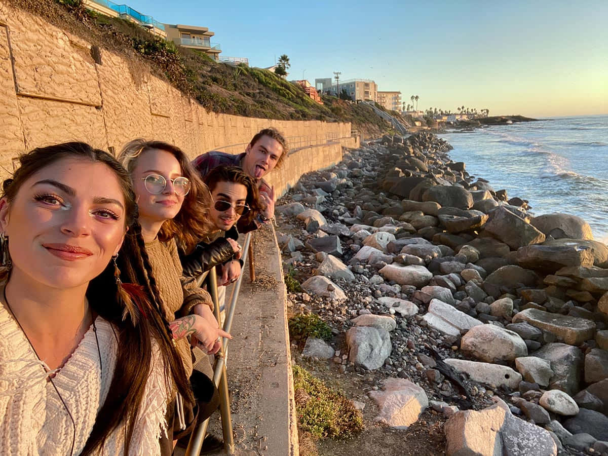 Sea Beach 桌布 壁紙 — 四位朋友在黃金時段的海岸懸崖上愉快地擺姿勢，海浪拍打著下方的岩石。
