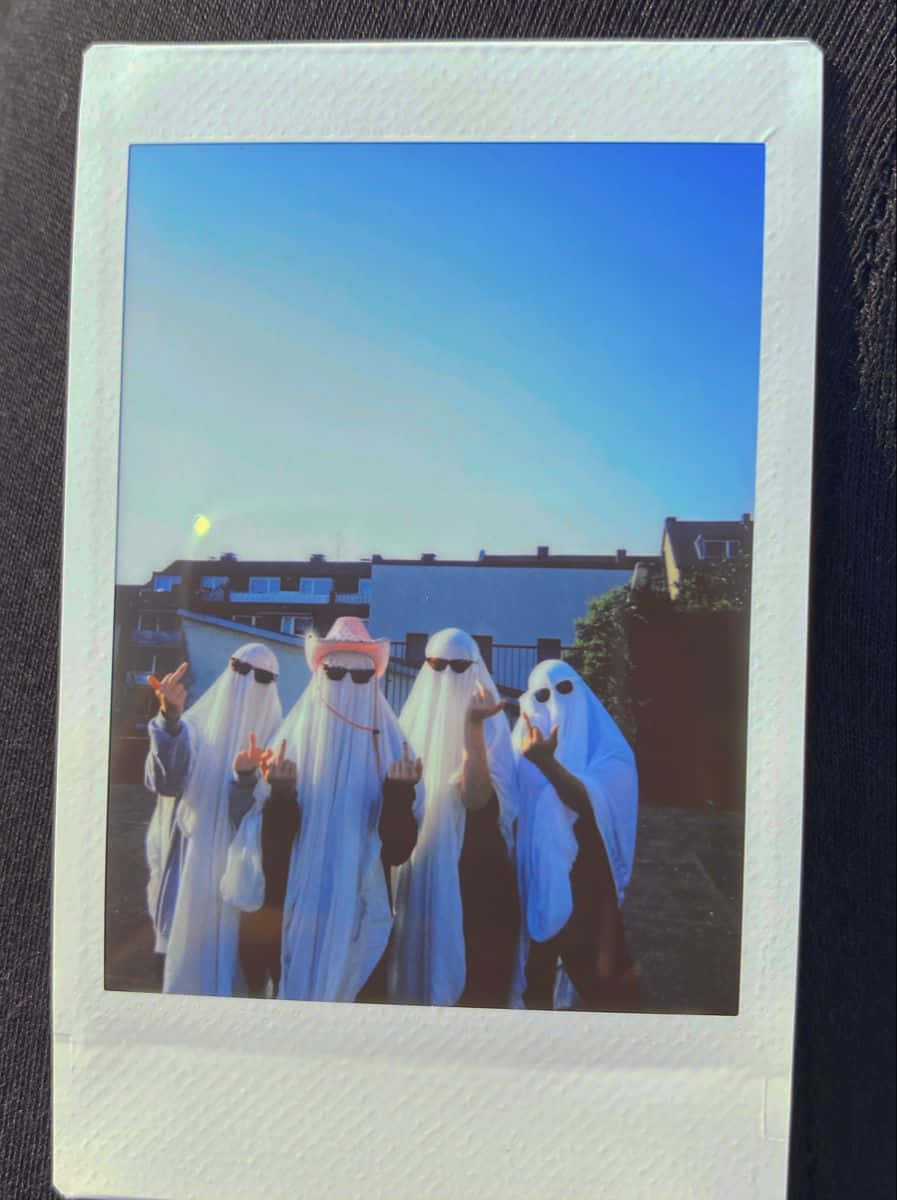 Aesthetic Polaroid 桌布 壁紙 — 四位朋友穿著鬼魂服裝，在日落時分晴朗的藍天下，在屋頂上俏皮地擺姿勢。
