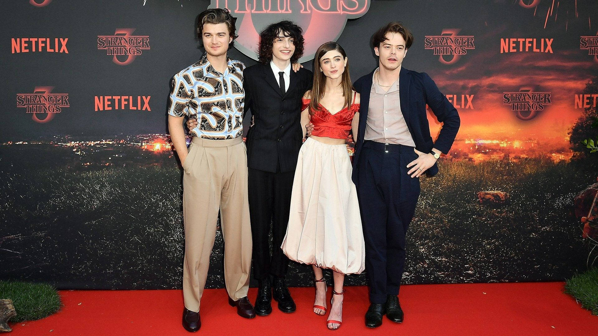 Joe Keery 桌布 壁紙 — 四位演員在Stranger Things宣傳背景（以熾熱日落景觀為特色）前自信地擺姿勢在紅地毯上。