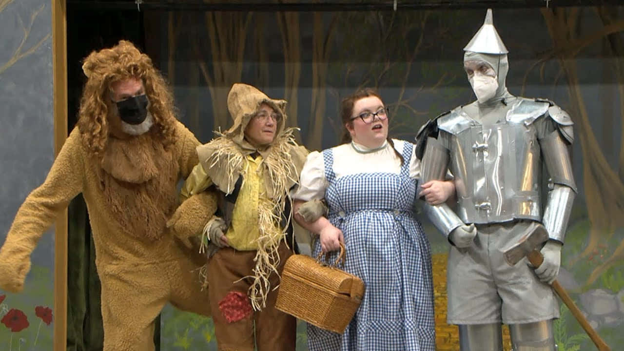 wizard of oz 桌布 壁紙 — 四位演員穿著綠野仙蹤服裝，在繪有森林背景的舞台上一起擺姿勢。