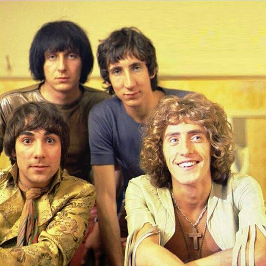 Rock 桌布 壁紙 — 四位男士留著1970年代髮型，穿著休閒服裝，在純黃色牆前一起擺姿勢。