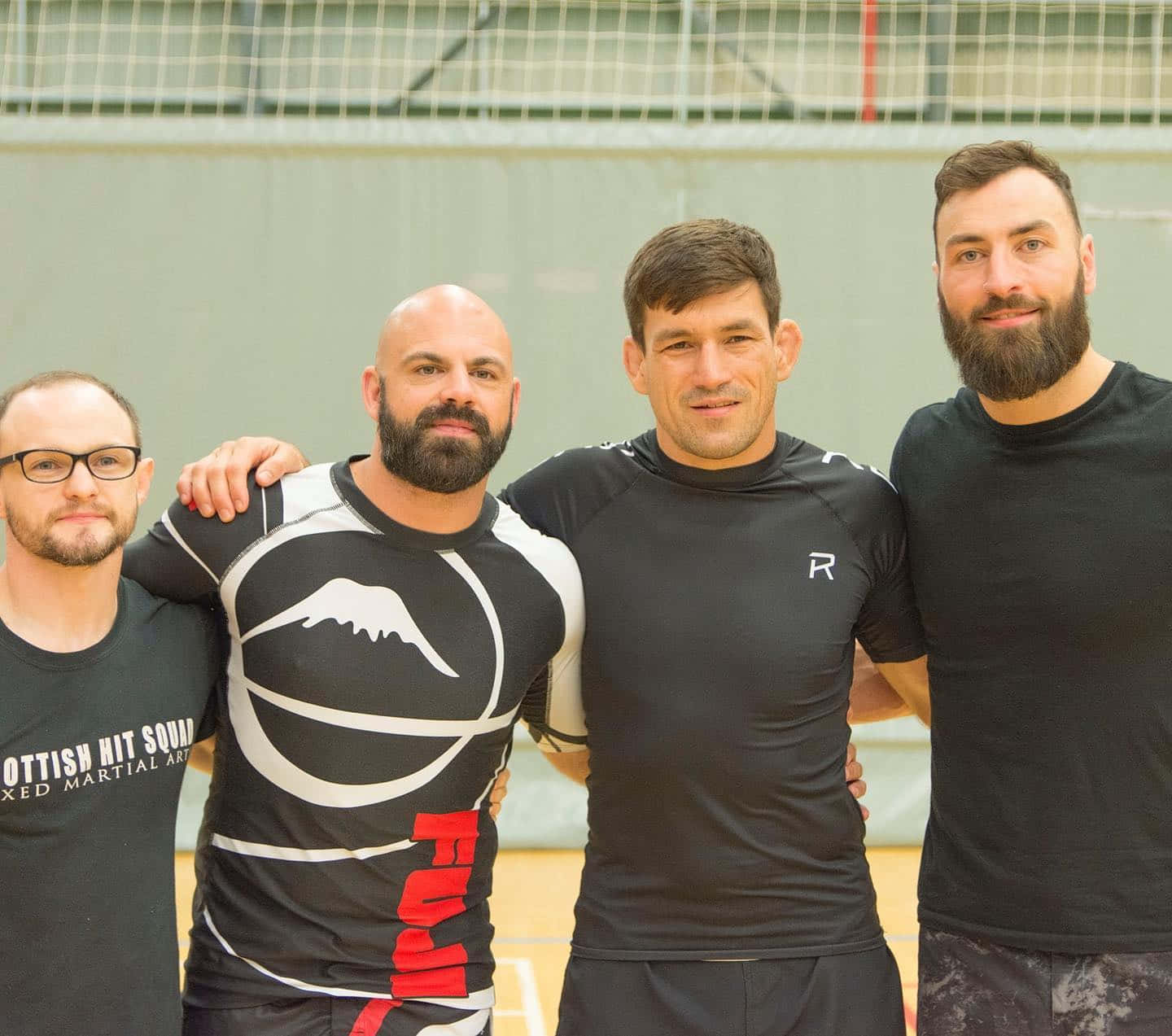 UFC 桌布 壁紙 — 四位留鬍鬚的男士穿著武術裝備，在體育館內自信地擺姿勢，手臂互相搭在對方身上。