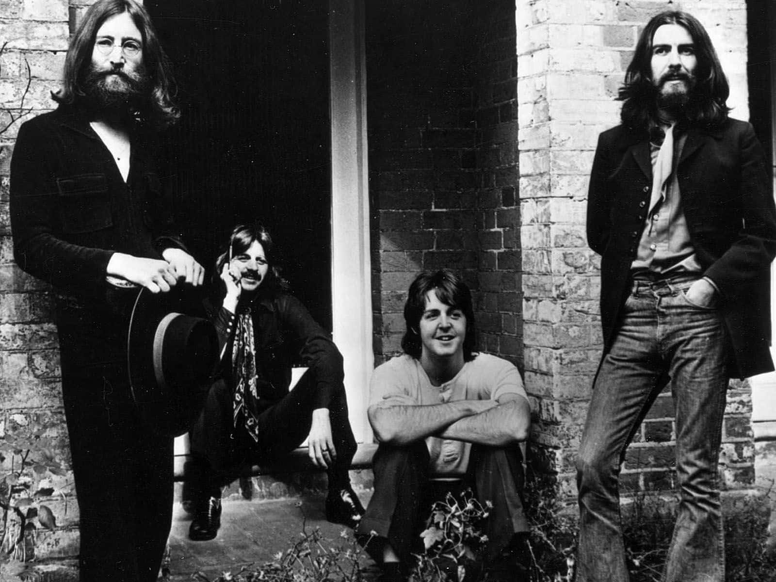 the beatles 桌布 壁紙 — 四位留鬍鬚的男子穿著復古服裝，在磚牆前隨意擺姿勢，是一張經典的黑白照片。
