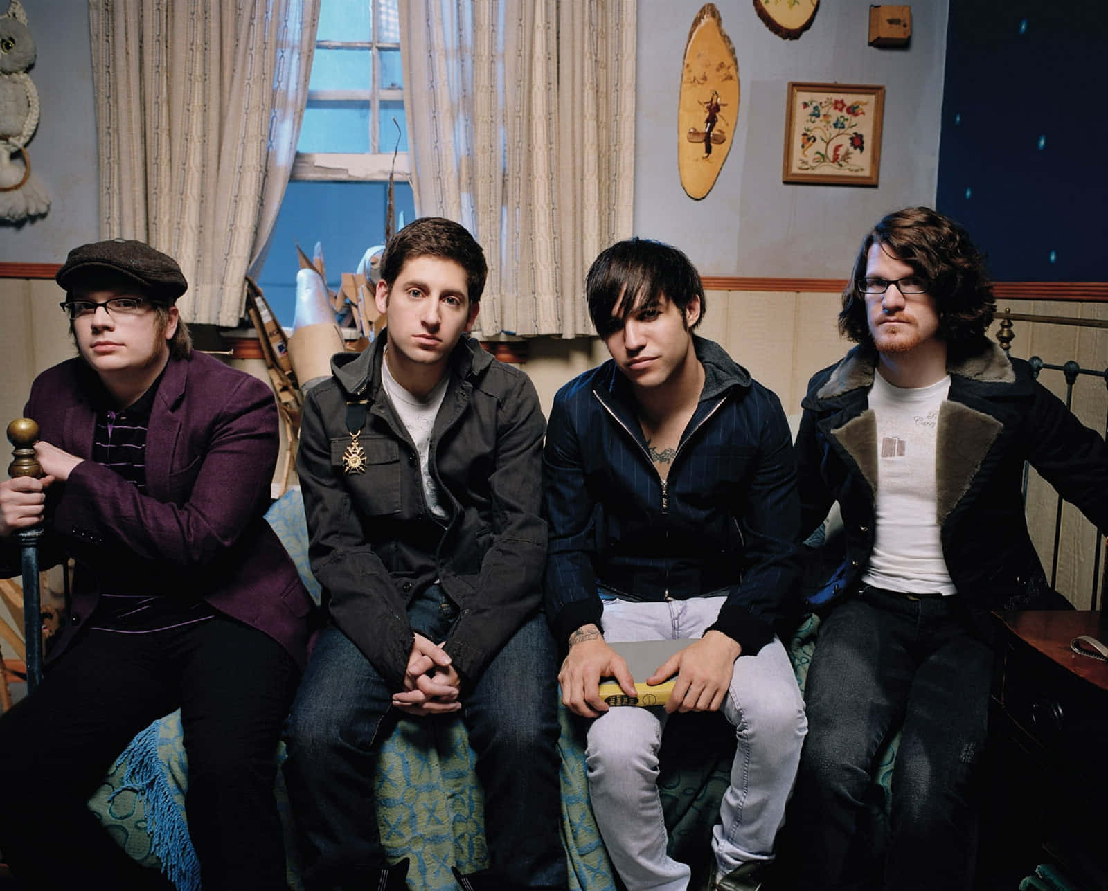 fall out boy 桌布 壁紙 — 四位穿著休閒服裝的男士一起坐在一張有圖案的沙發上，房間光線溫暖，裝潢不拘一格，帶有復古風格。