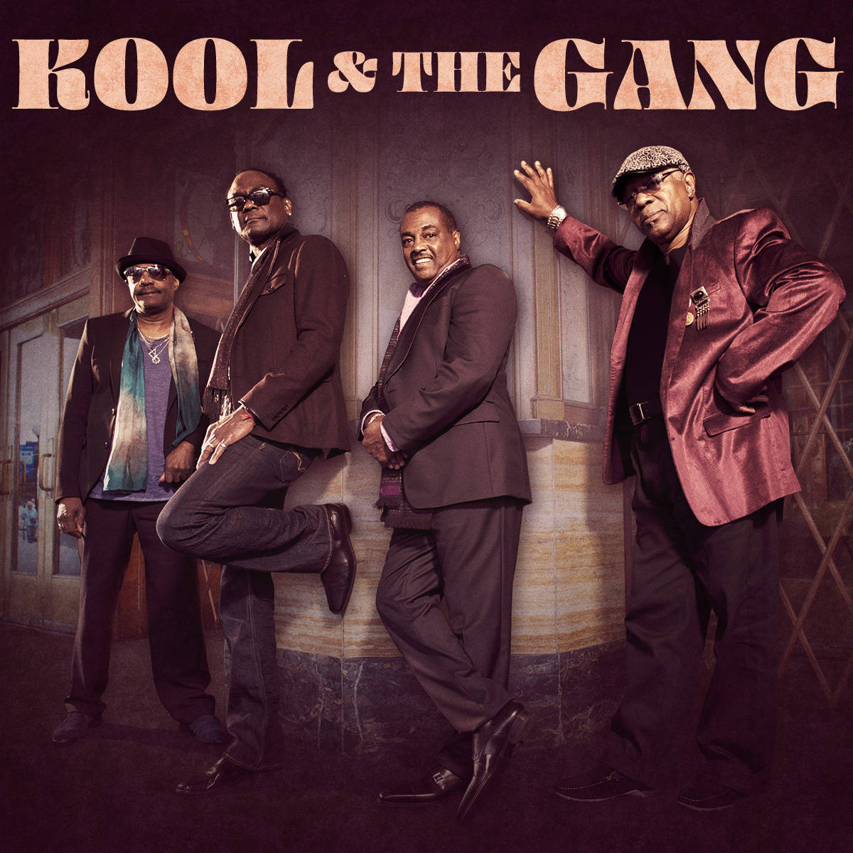 Kool And The Gang 桌布 壁紙 — 四位穿著時尚西裝的男士在溫暖燈光下，自信地以復古建築外牆為背景擺姿勢。