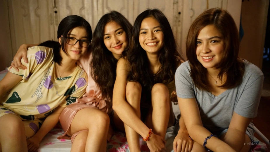 Teenage Girls 桌布 壁紙 — 四位穿著睡衣的年輕女性微笑著緊密地坐在一張床上，房間內燈光溫暖。