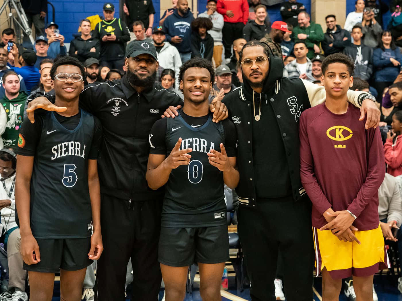 Bronny James 桌布 壁紙 — 四位籃球運動員和教練在體育館球場上一起擺姿勢，背景有群眾觀看。