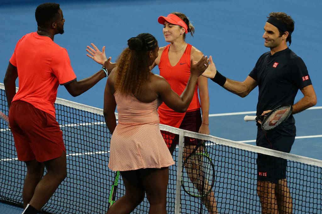 Tennis 桌布 壁紙 — 四位網球運動員在明亮的體育場燈光下，在充滿活力的藍色球場上隔網擊掌。