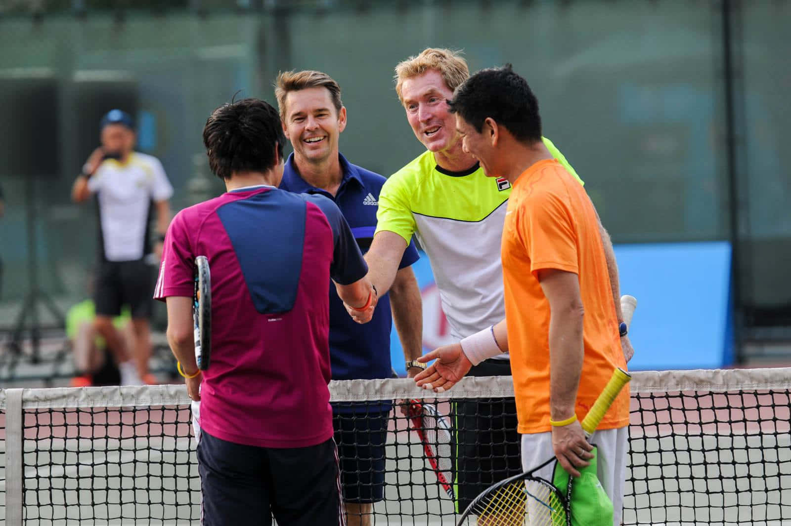 Tennis 桌布 壁紙 — 四位網球選手在比賽結束後隔網握手，笑容燦爛，穿著鮮豔的運動服。