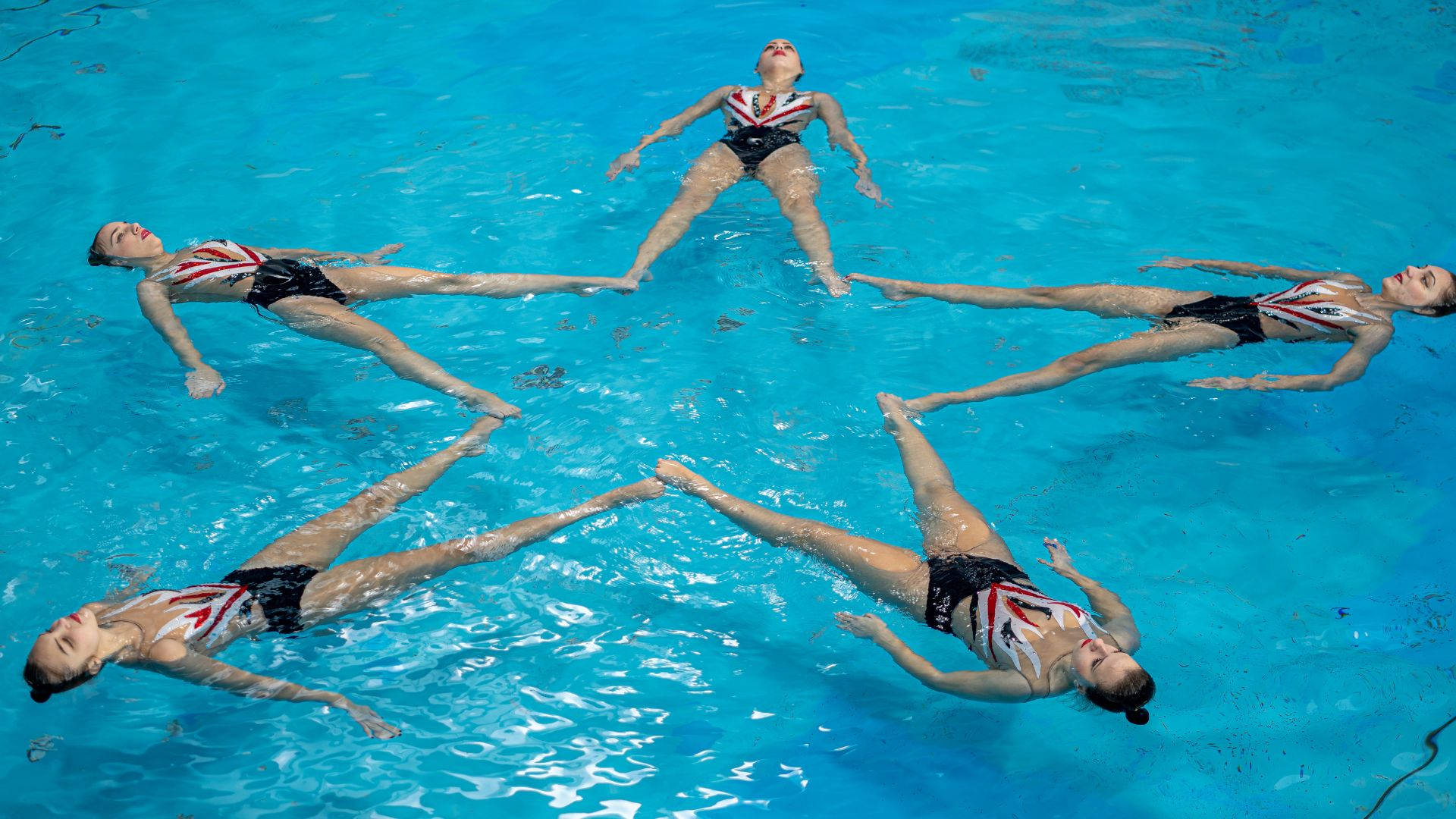 Swimming 桌布 壁紙 — 四位花式游泳運動員在明亮的藍色泳池中優雅漂浮，伸展手臂和雙腿形成星形圖案。
