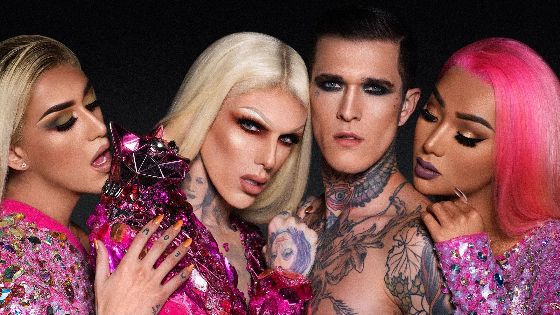 Jeffree Star 桌布 壁紙 — 四位華麗的變裝表演者身穿閃閃發光的粉紅色服裝，在黑色背景前圍繞一個閃亮的粉紅色貓雕像擺出強烈的姿勢。