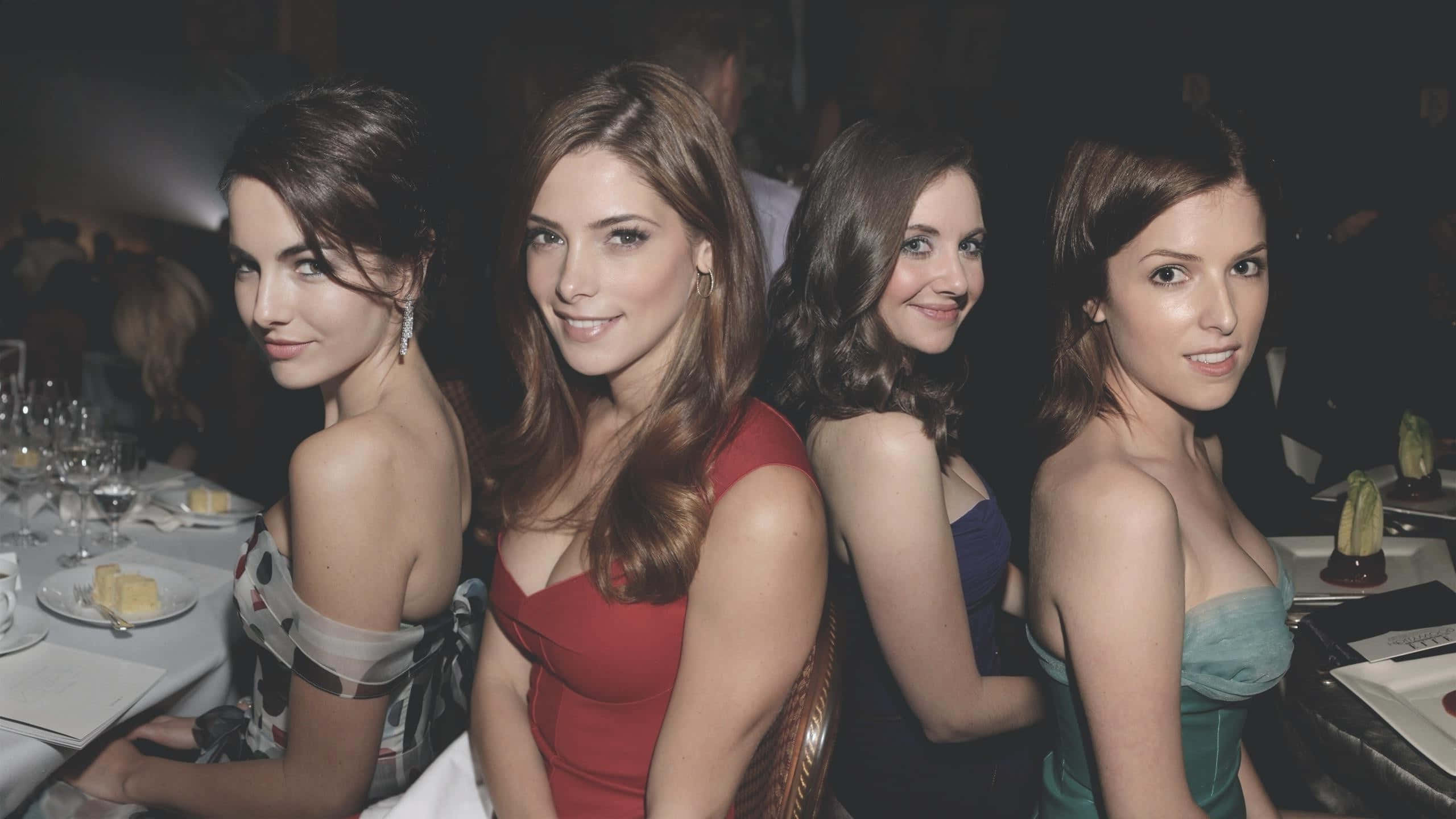 Camilla Belle 桌布 壁紙 — 四位衣著優雅的女士坐在燈光昏暗的正式晚餐桌旁，對著鏡頭微笑。
