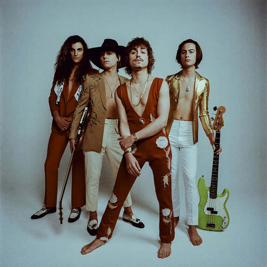 band 桌布 壁紙 — 四位赤腳的時尚音樂家穿著70年代華麗服裝，在樸素的攝影棚背景下自信地擺出拿著吉他的姿勢。