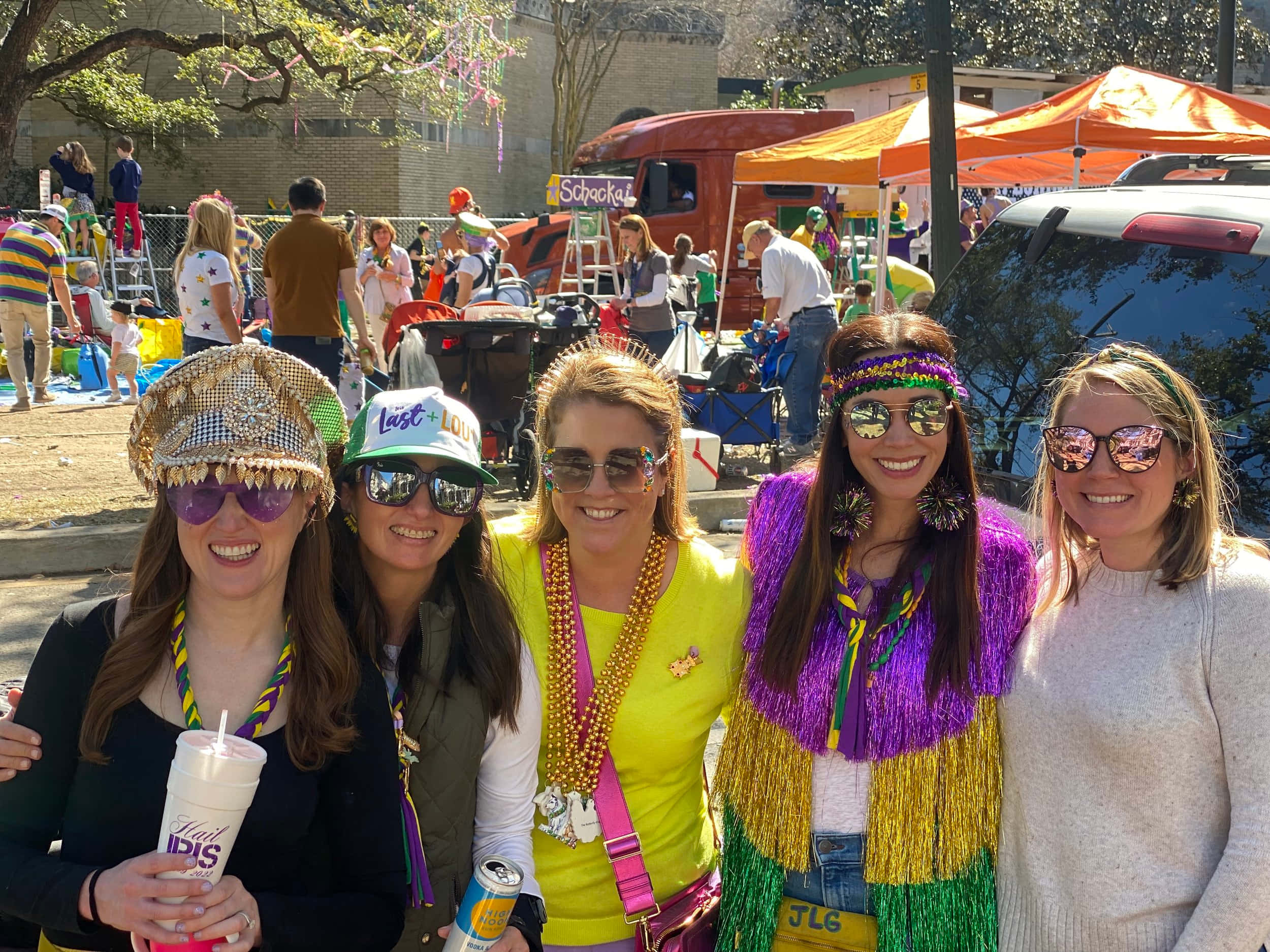 Mardi Gras 桌布 壁紙 — 四位身穿節慶狂歡節服飾的女性在熱鬧的戶外遊行中燦爛微笑，背景是色彩繽紛的帳篷和人群。