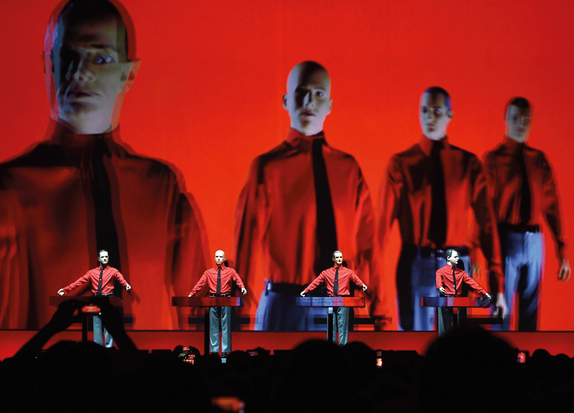 band 桌布 壁紙 — 四位身穿紅衫黑領帶的表演者在舞台上，在一個顯示他們面孔的巨大紅色螢幕下彈奏鍵盤。
