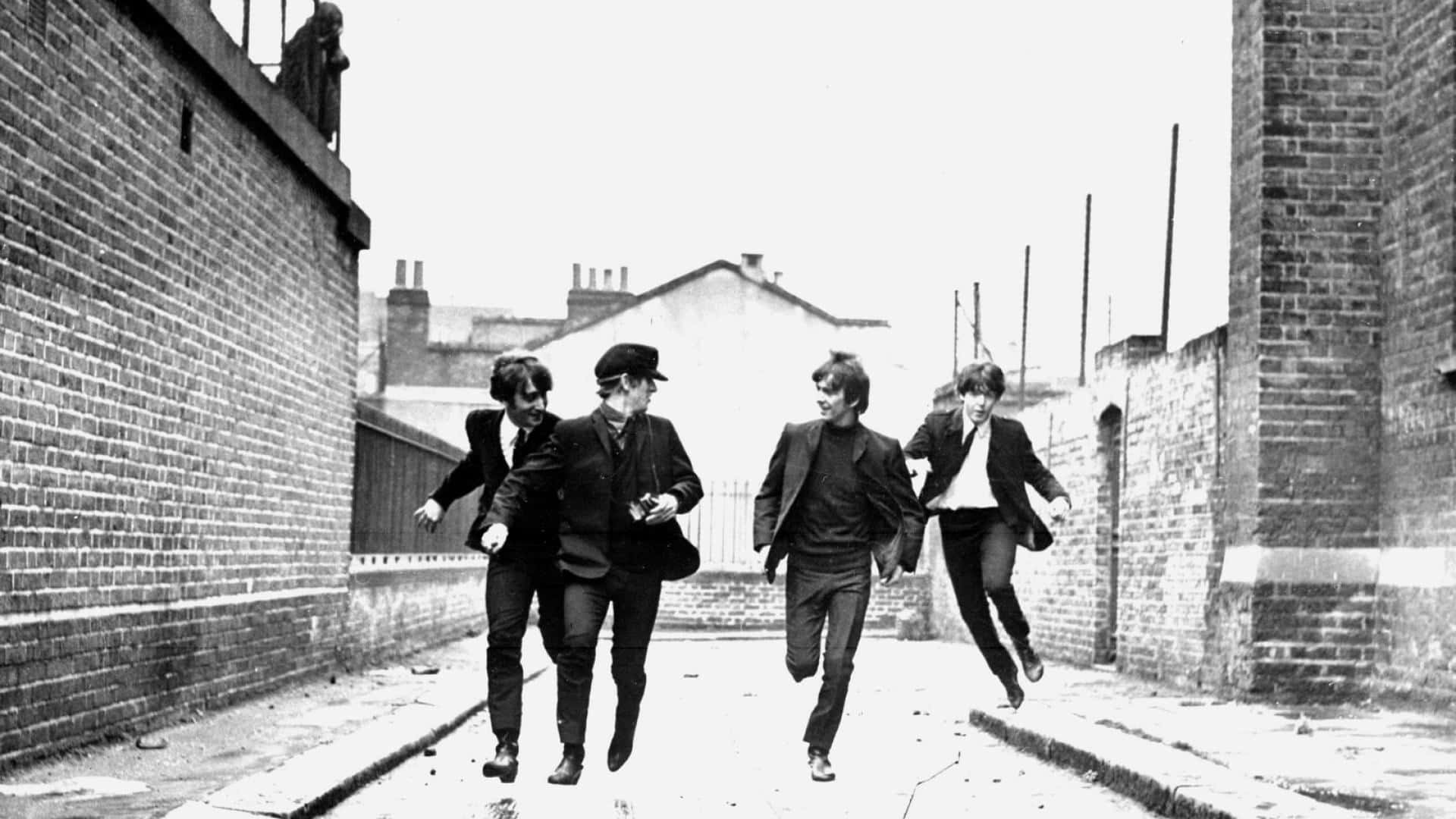 the beatles 桌布 壁紙 — 四位身穿西裝的男子在一張經典黑白照片中，沿著狹窄的磚砌小巷歡快地跳躍。