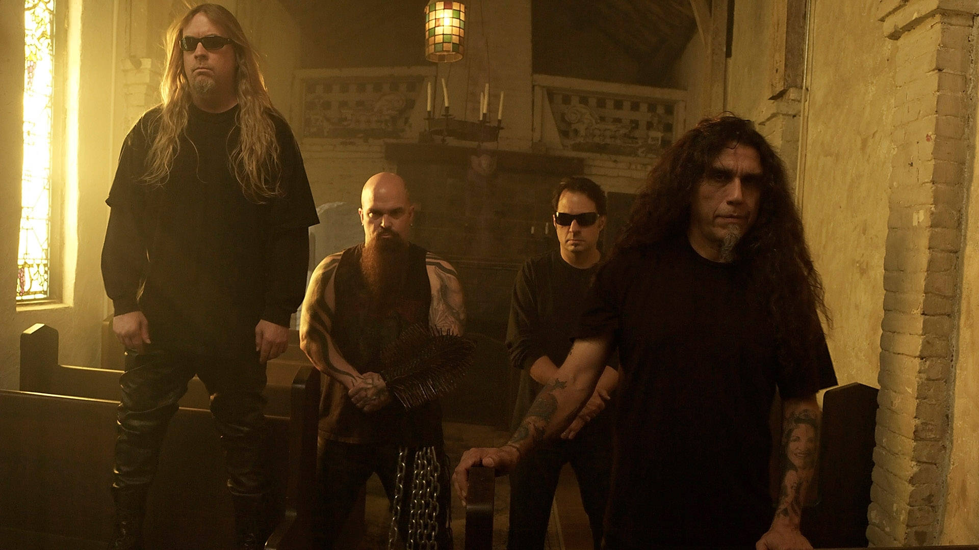 Slayer 桌布 壁紙 — 四位長髮及紋身的重金屬音樂家，莊嚴地站在光線昏暗、有彩繪玻璃窗的教堂內。
