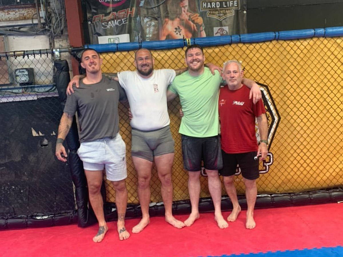 UFC 桌布 壁紙 — 四位面帶微笑、身穿運動服的男士在紅色軟墊上的MMA拳籠內一起擺姿勢。